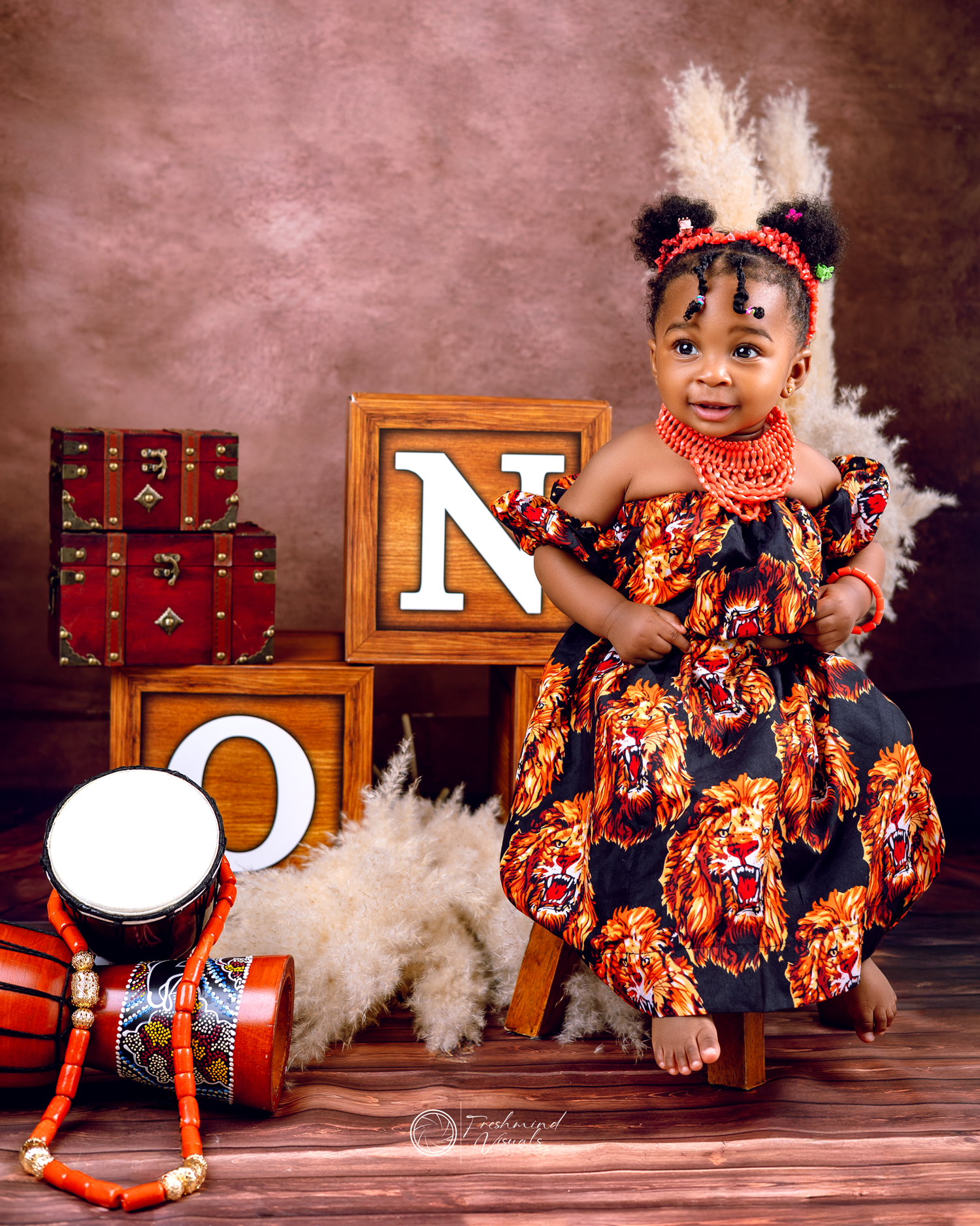 First birthday photos with orange floral outfit and wooden letter decorations against dark backdrop.