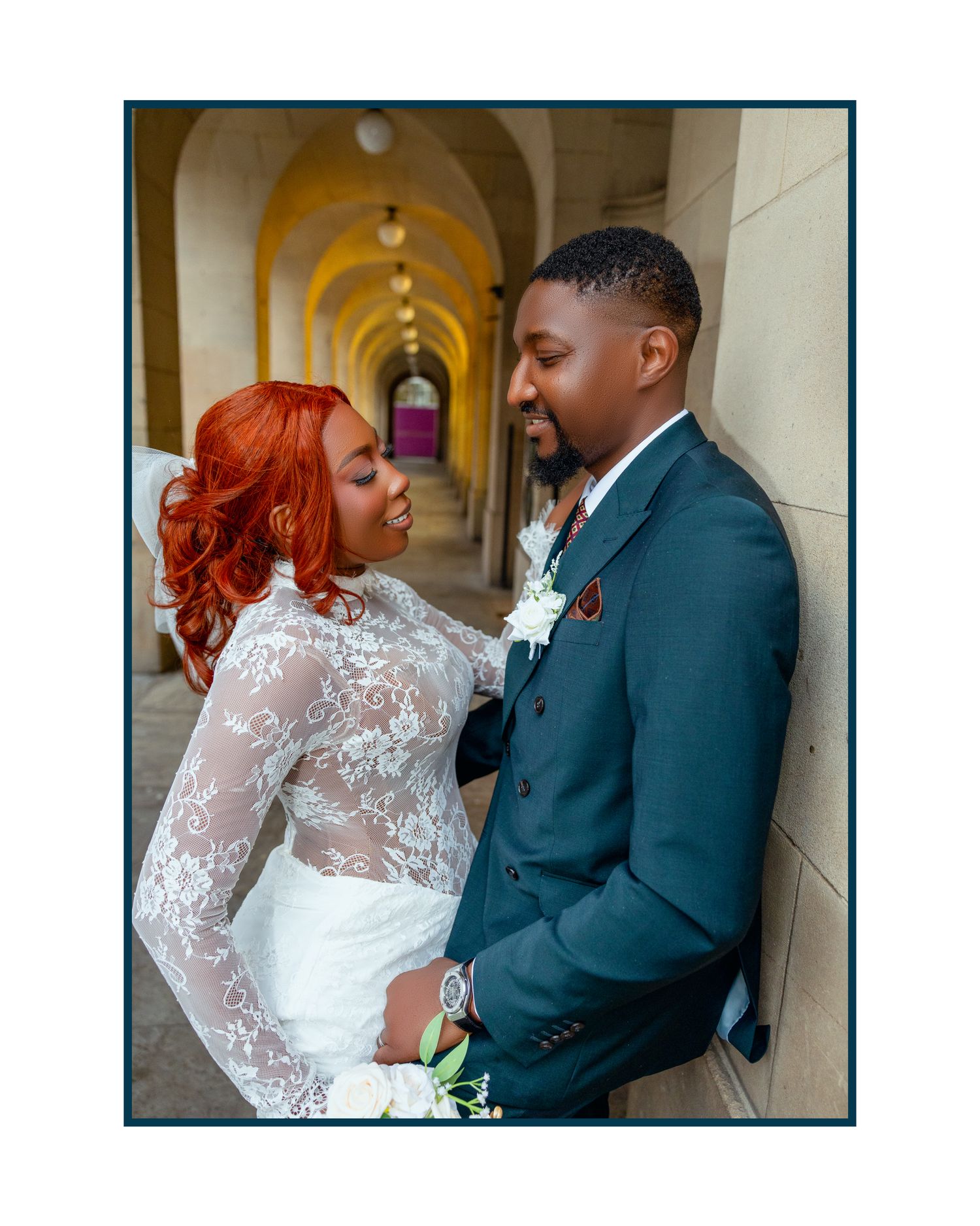 A couple in wedding attire share intimate moments in an elegant hallway with arched architecture.