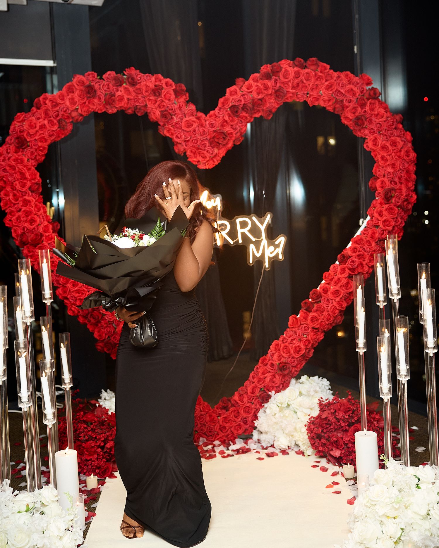 Romantic proposal setting with red rose heart decorations and white candle lighting.