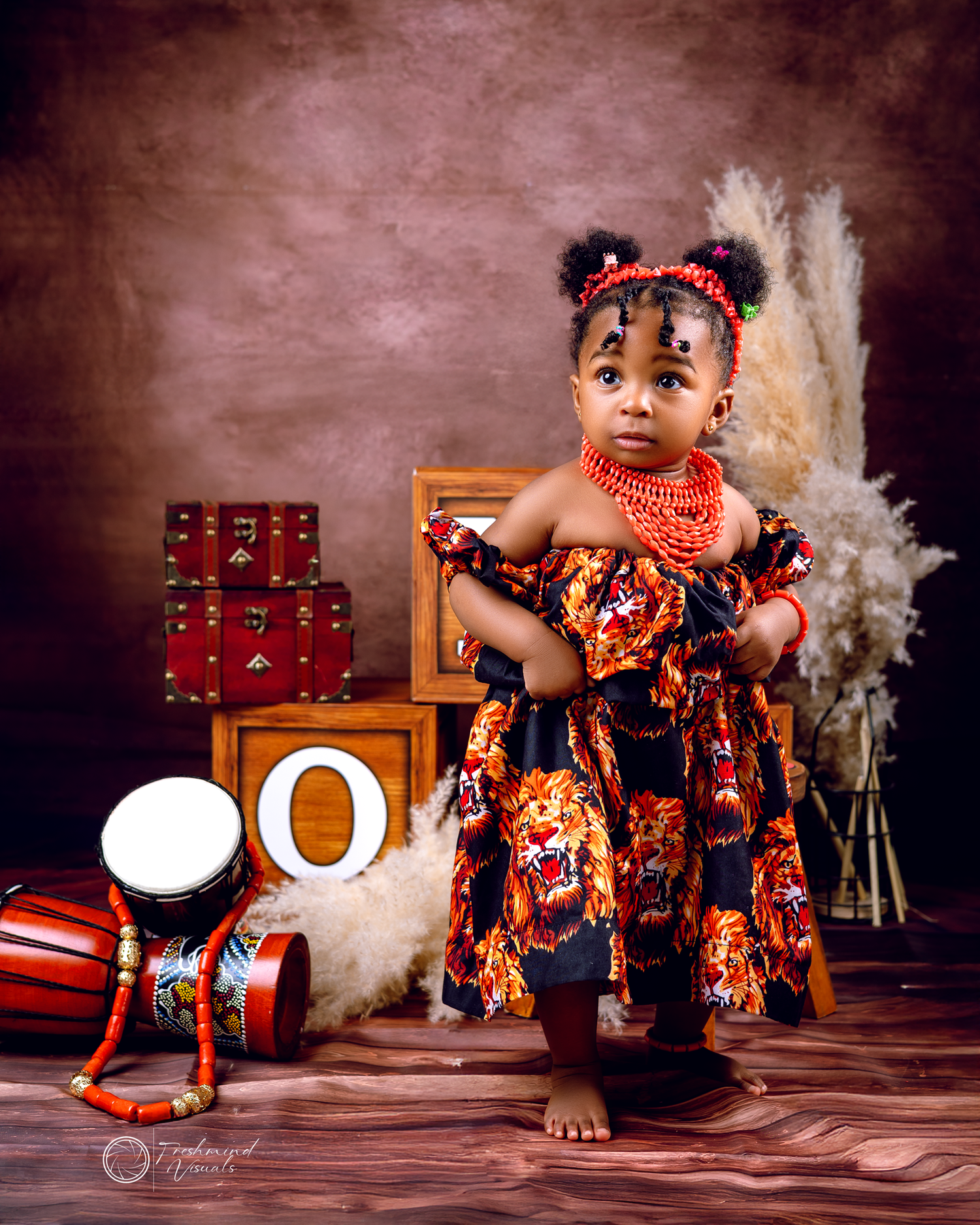 Toddler in colorful African print dress poses with decorative props and pampas grass.