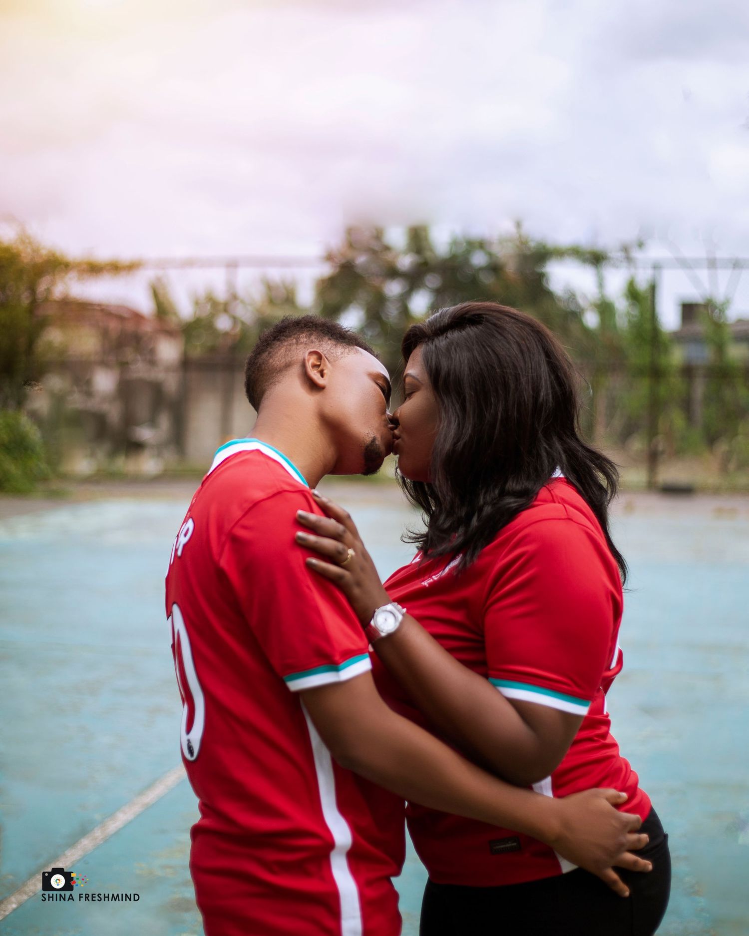 A couple in matching red jerseys sharing an intimate moment by the water during a photo session.