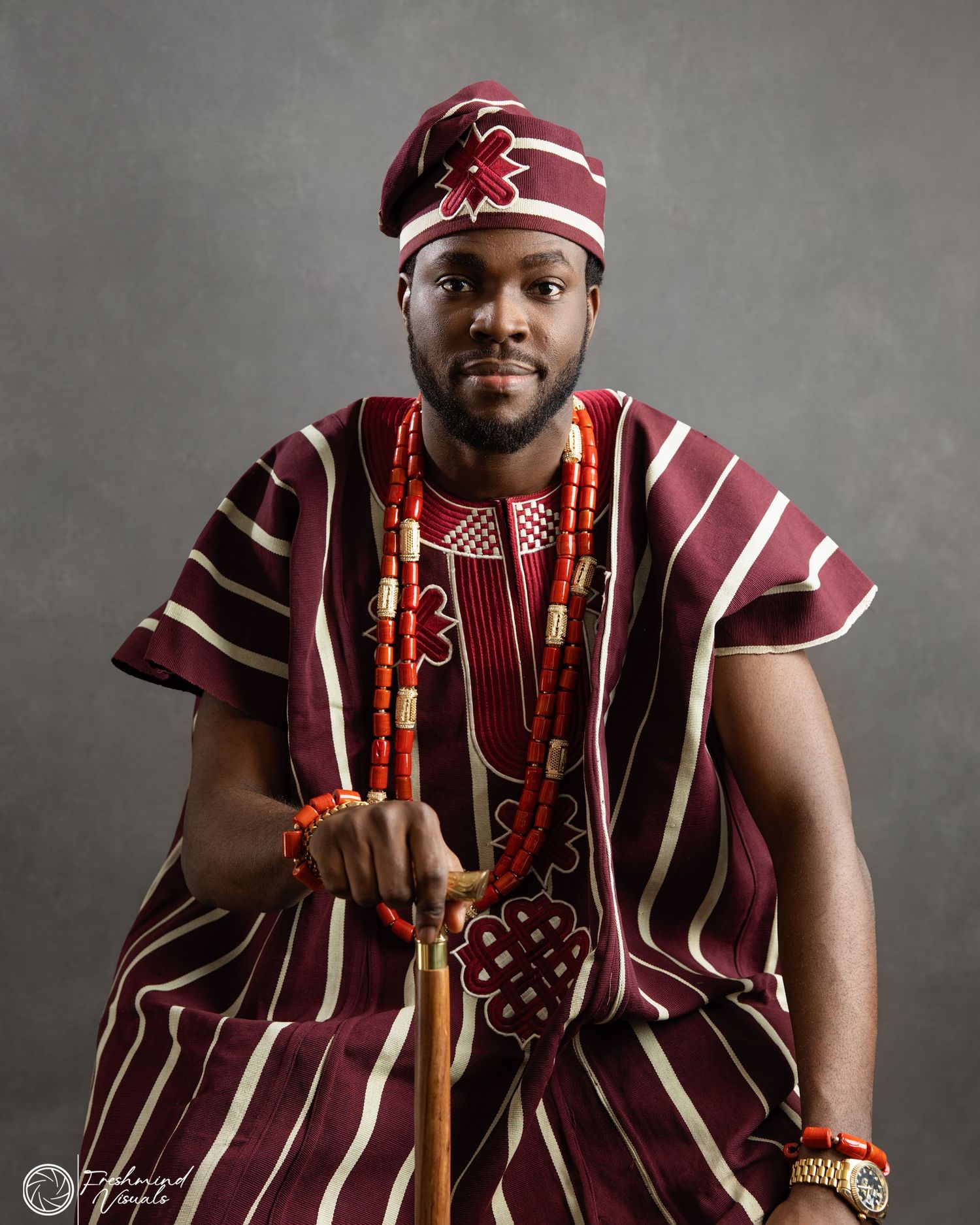 Traditional Nigerian wedding attire with burgundy striped agbada and coral beads.