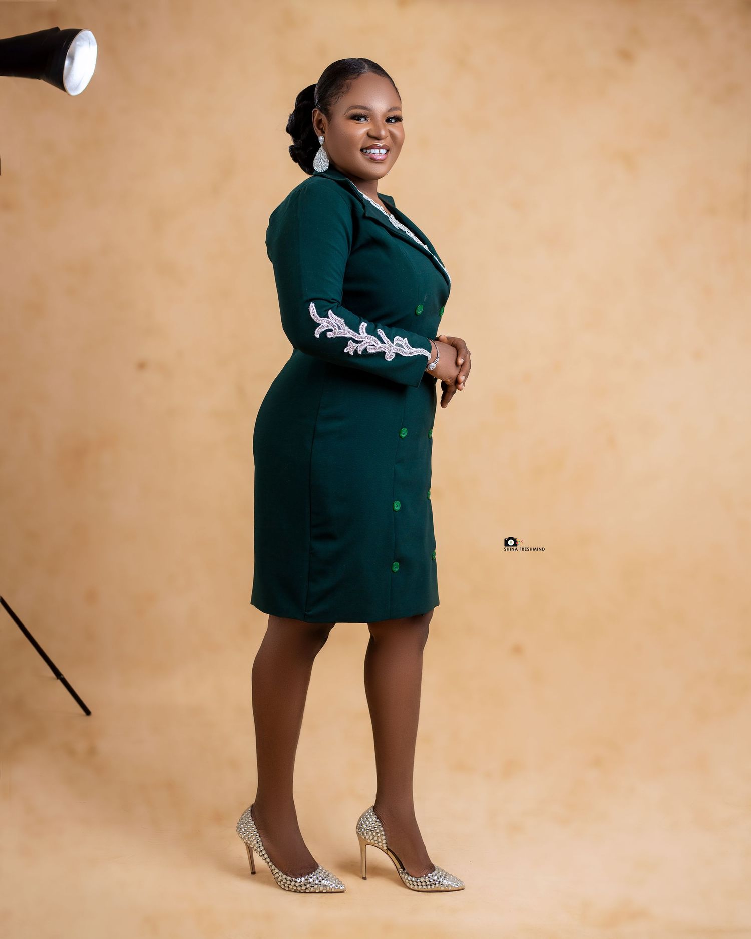 Full-length portrait of someone in an elegant green dress with white embellishments and metallic heels.
