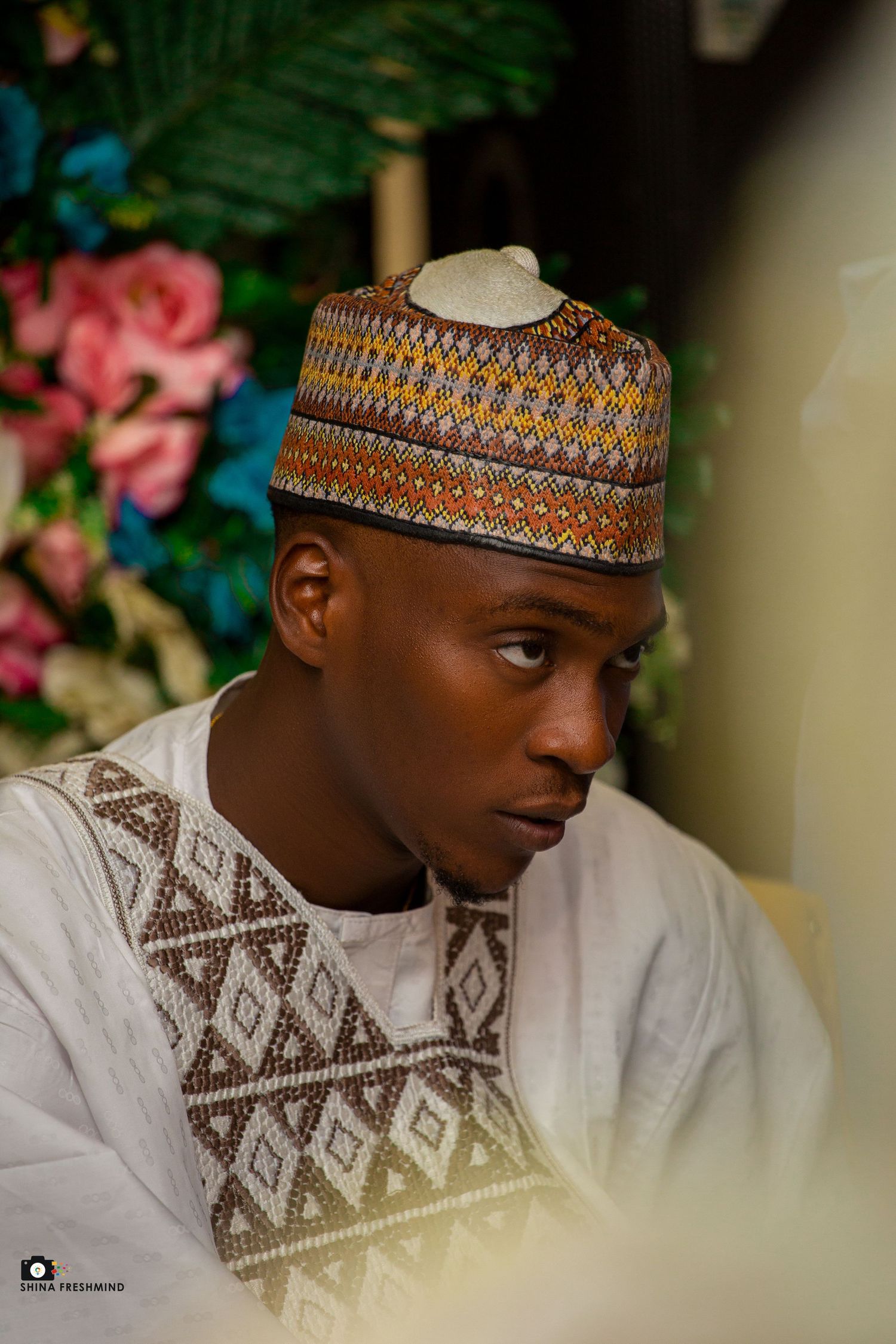 Groom wearing traditional white embroidered attire with patterned cap.