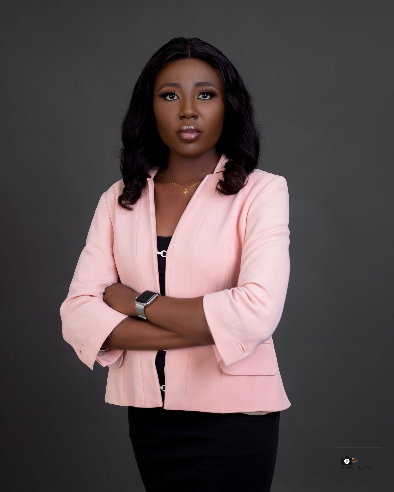 Professional studio portrait of a person wearing a pink blazer and black top against a dark background.