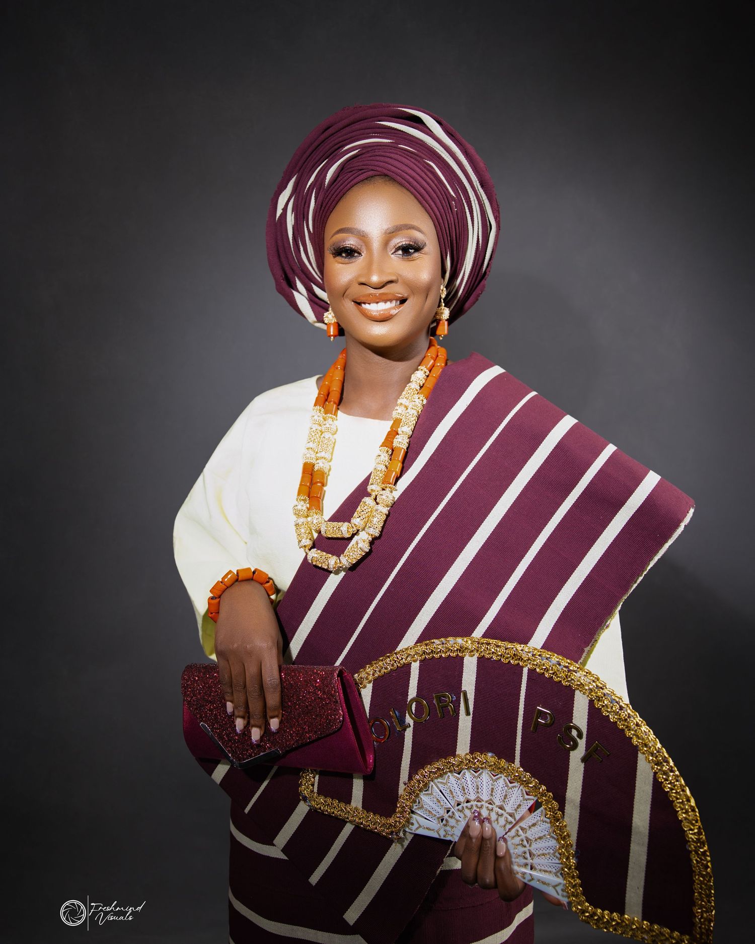 Elegant Nigerian traditional outfit with burgundy striped fabric and gold accents.