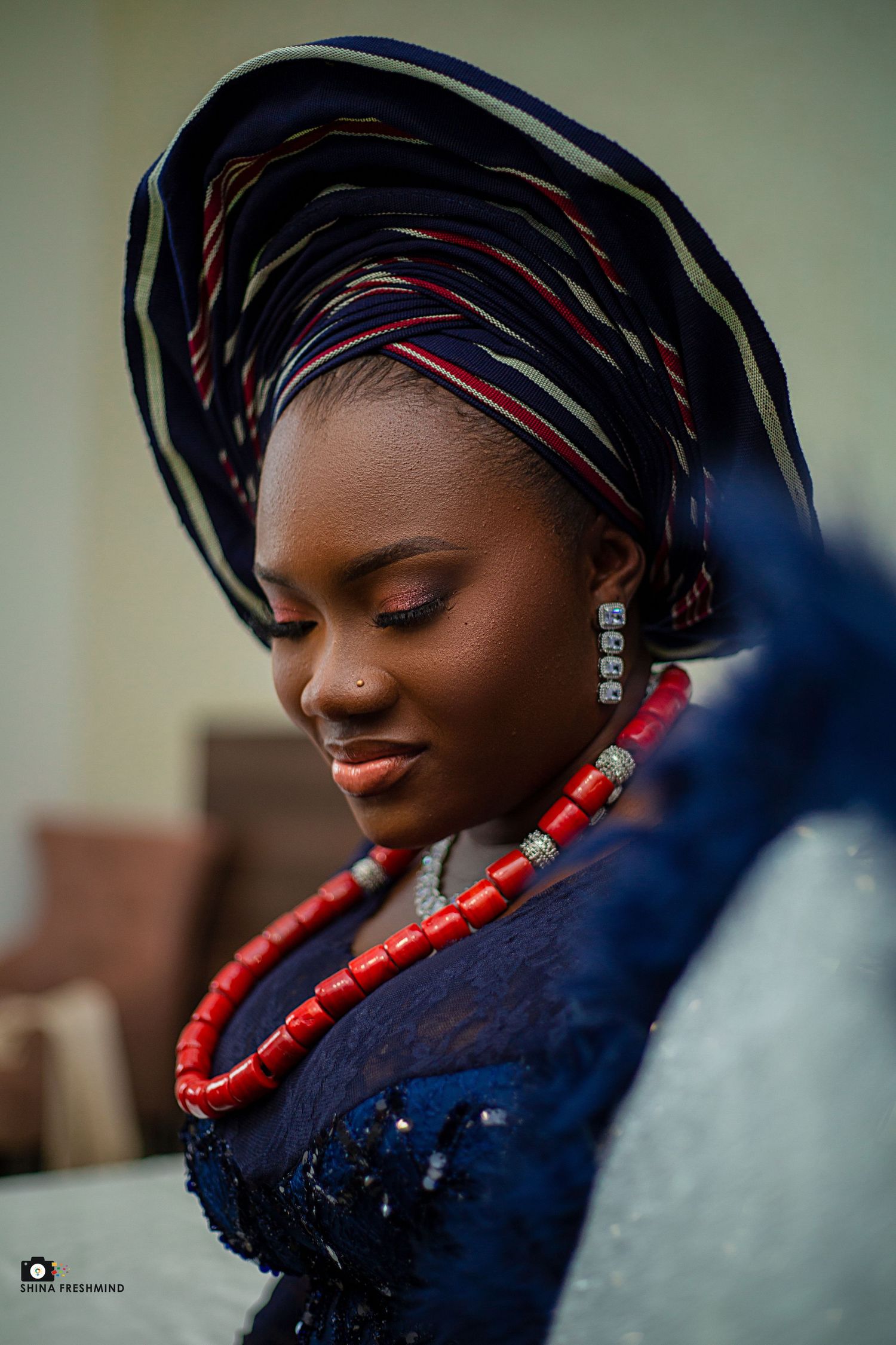 Traditional Nigerian headwrap and coral beaded necklace styled with navy attire.