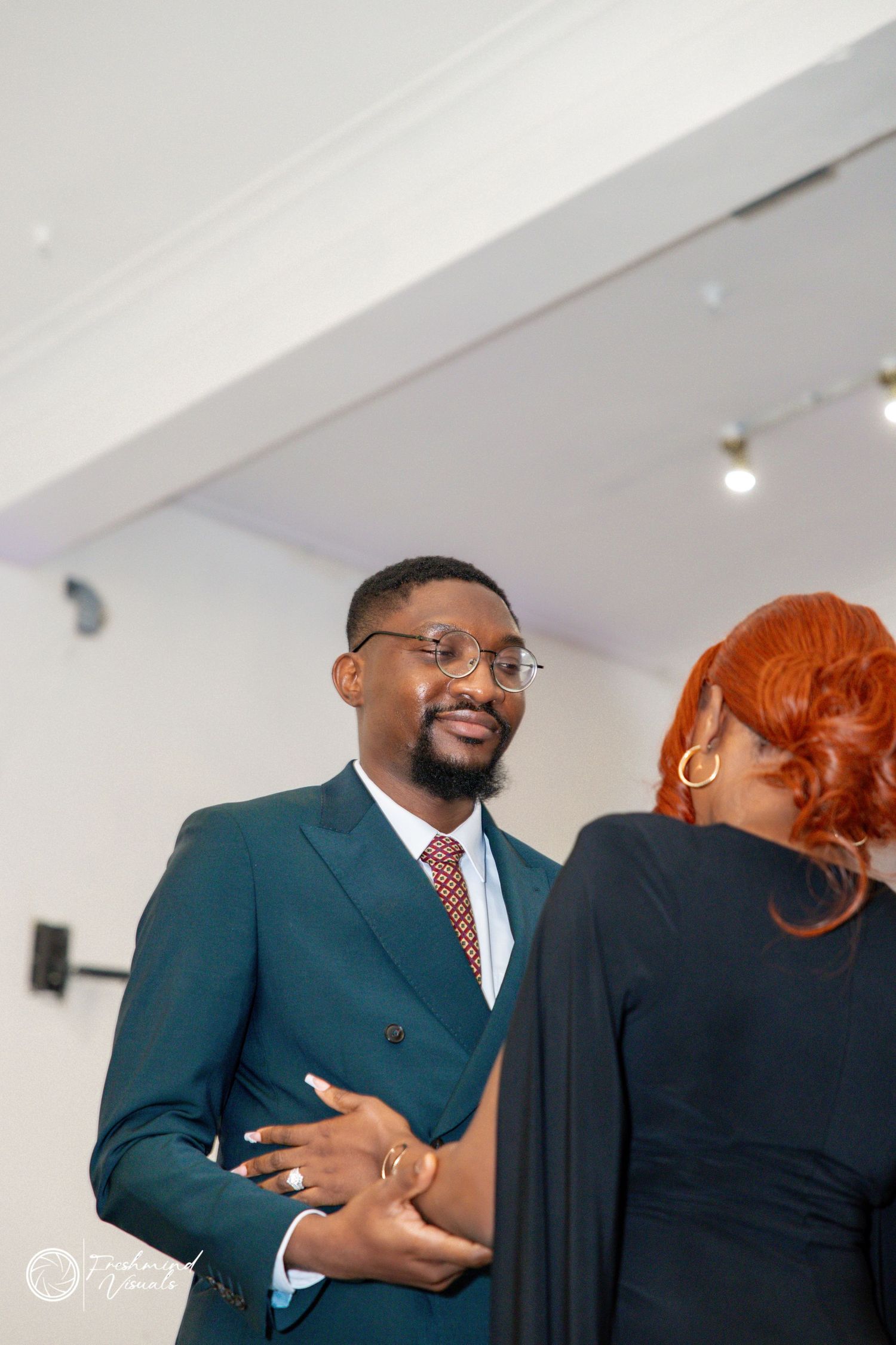 Professional interaction between two people in an office setting, with one wearing a teal suit and red tie.