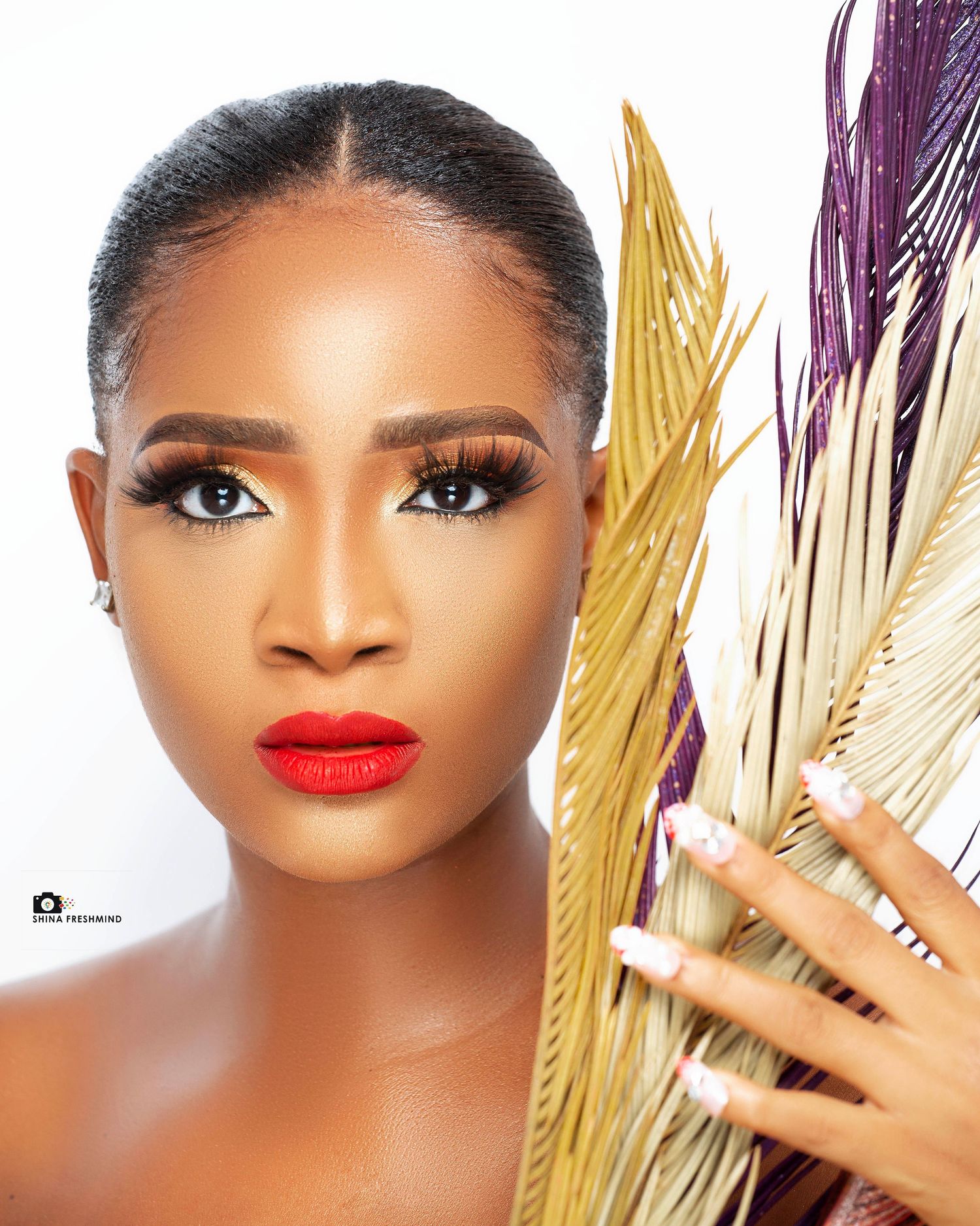 Artistic beauty portrait with gold accents, dramatic makeup and red lips against white background.