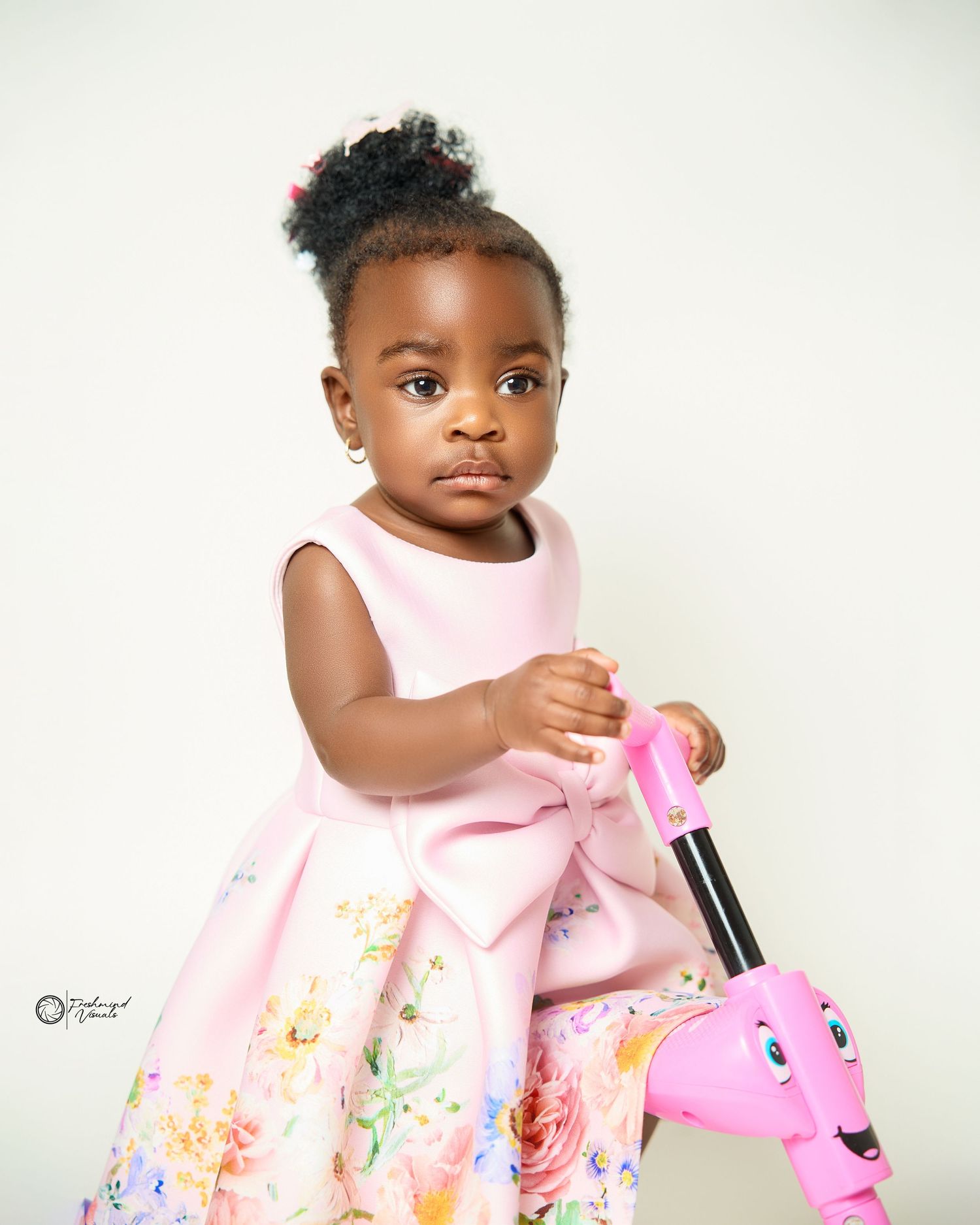 Baby photoshoot featuring pink floral dress against white background.