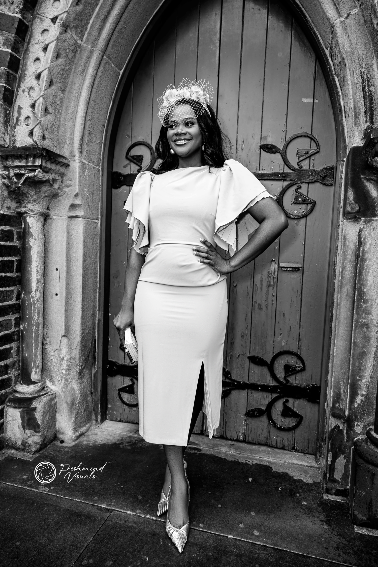 Elegant white dress photoshoot against rustic archway and wooden doors.