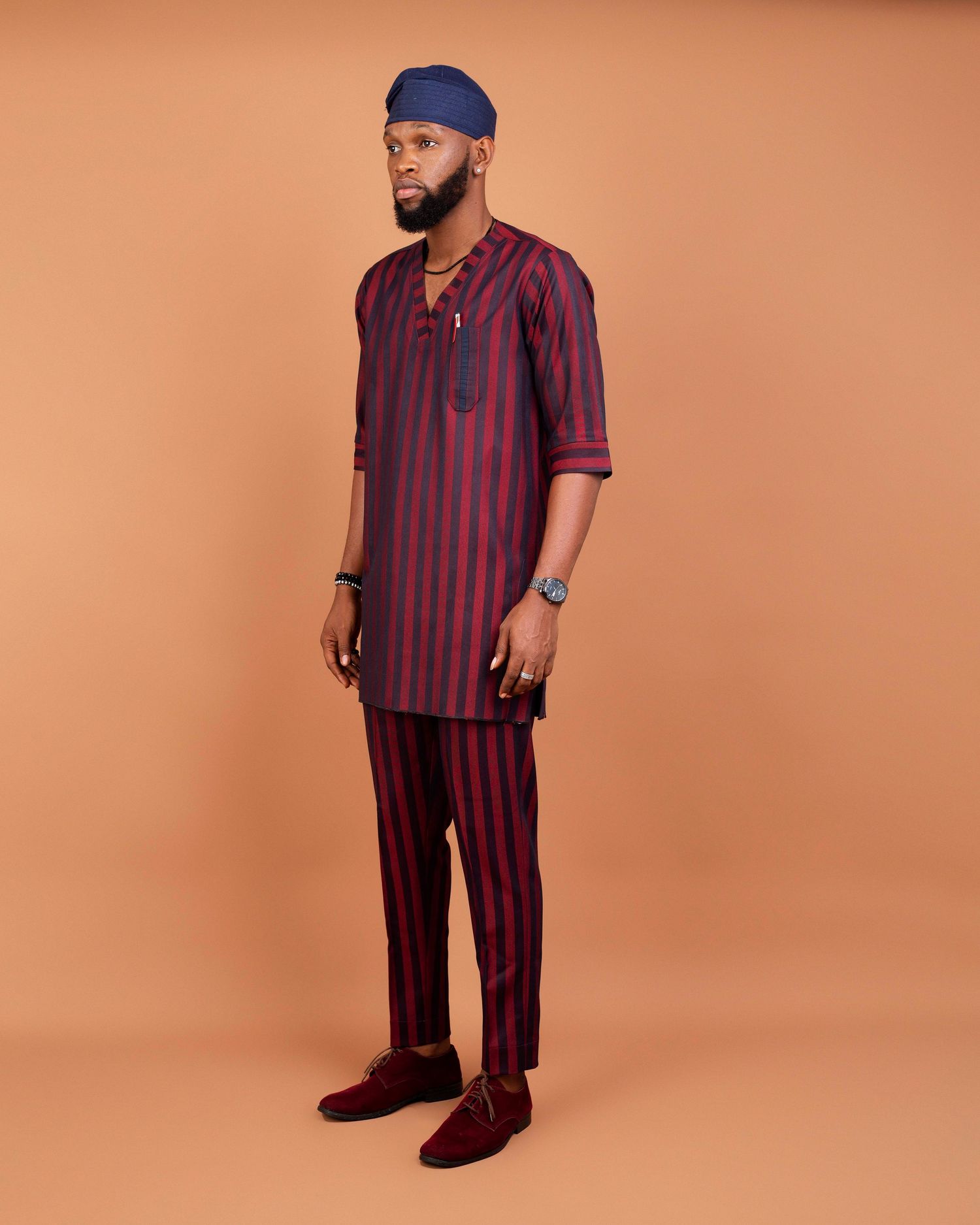 Portrait of someone in burgundy striped traditional African attire against orange background.