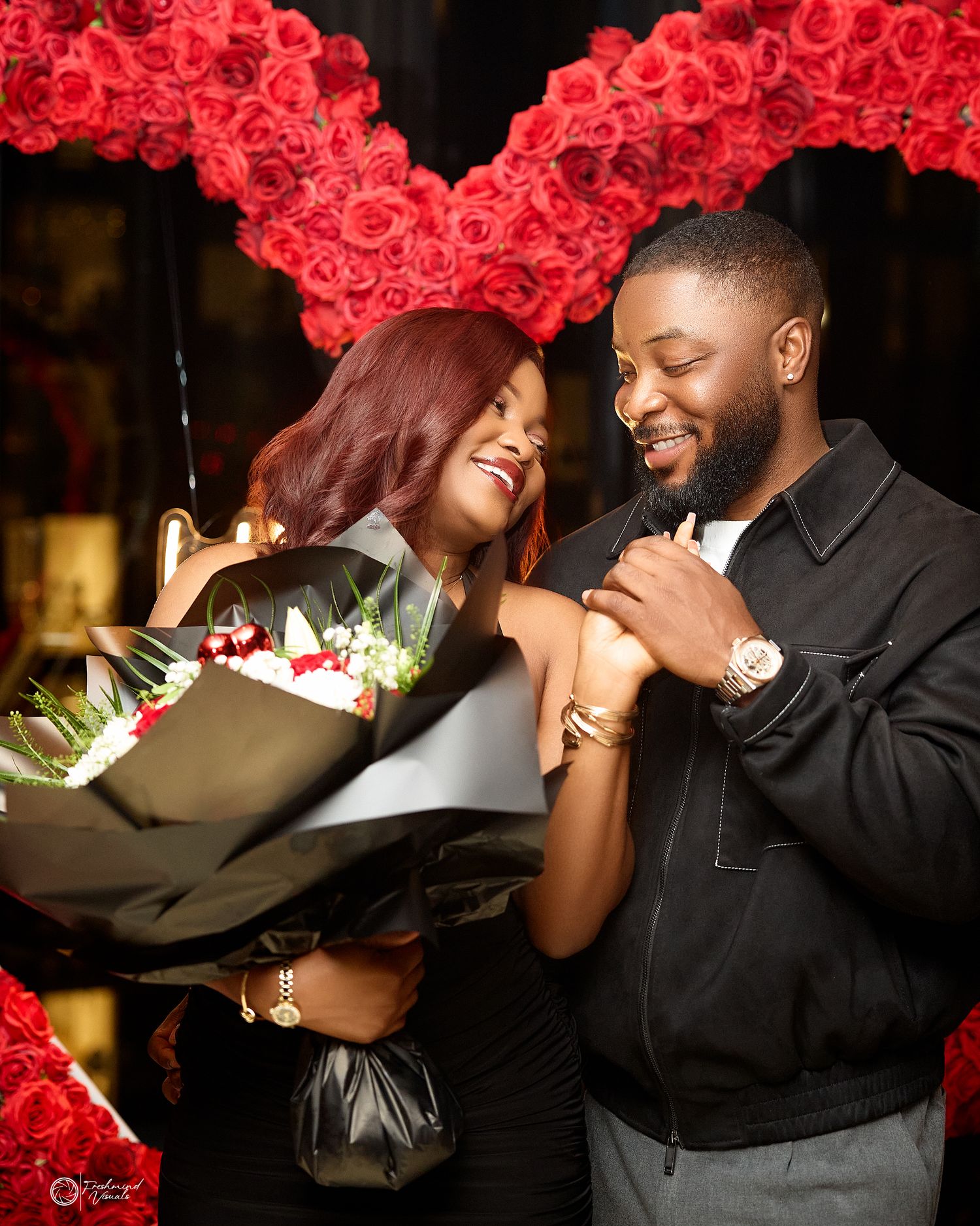 Couple sharing intimate moments under an arch of red roses in an elegant setting.