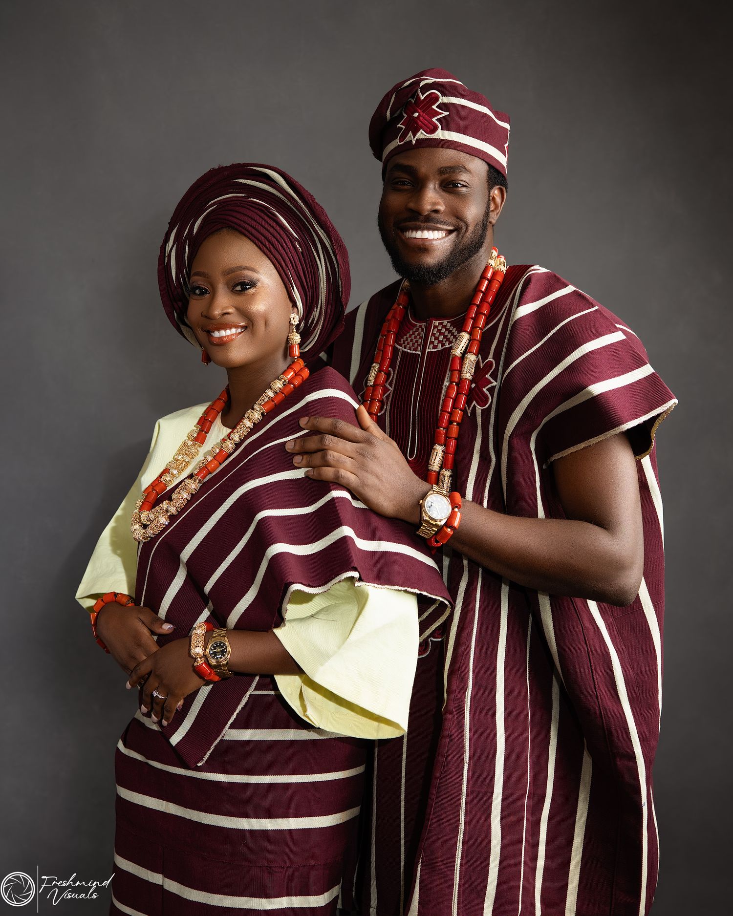 Traditional Nigerian couple in burgundy and white striped agbada attire during a photo session.