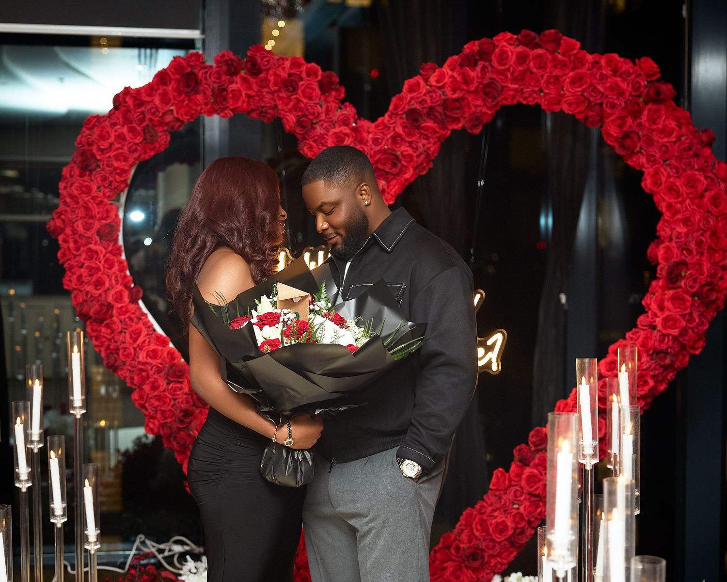 Intimate proposal moment under arch of red roses with white candles.