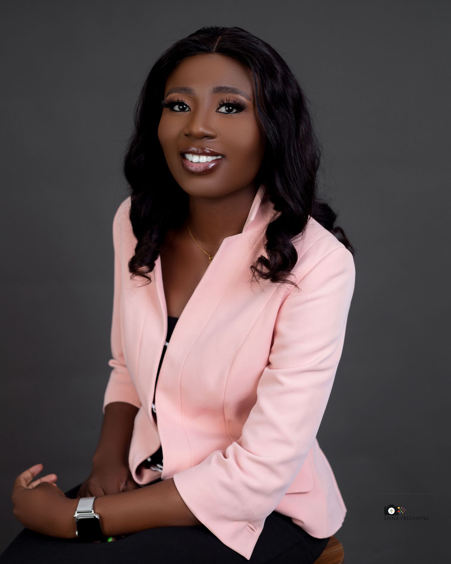 Studio portrait of a person in a pink blazer against a dark background with professional lighting.
