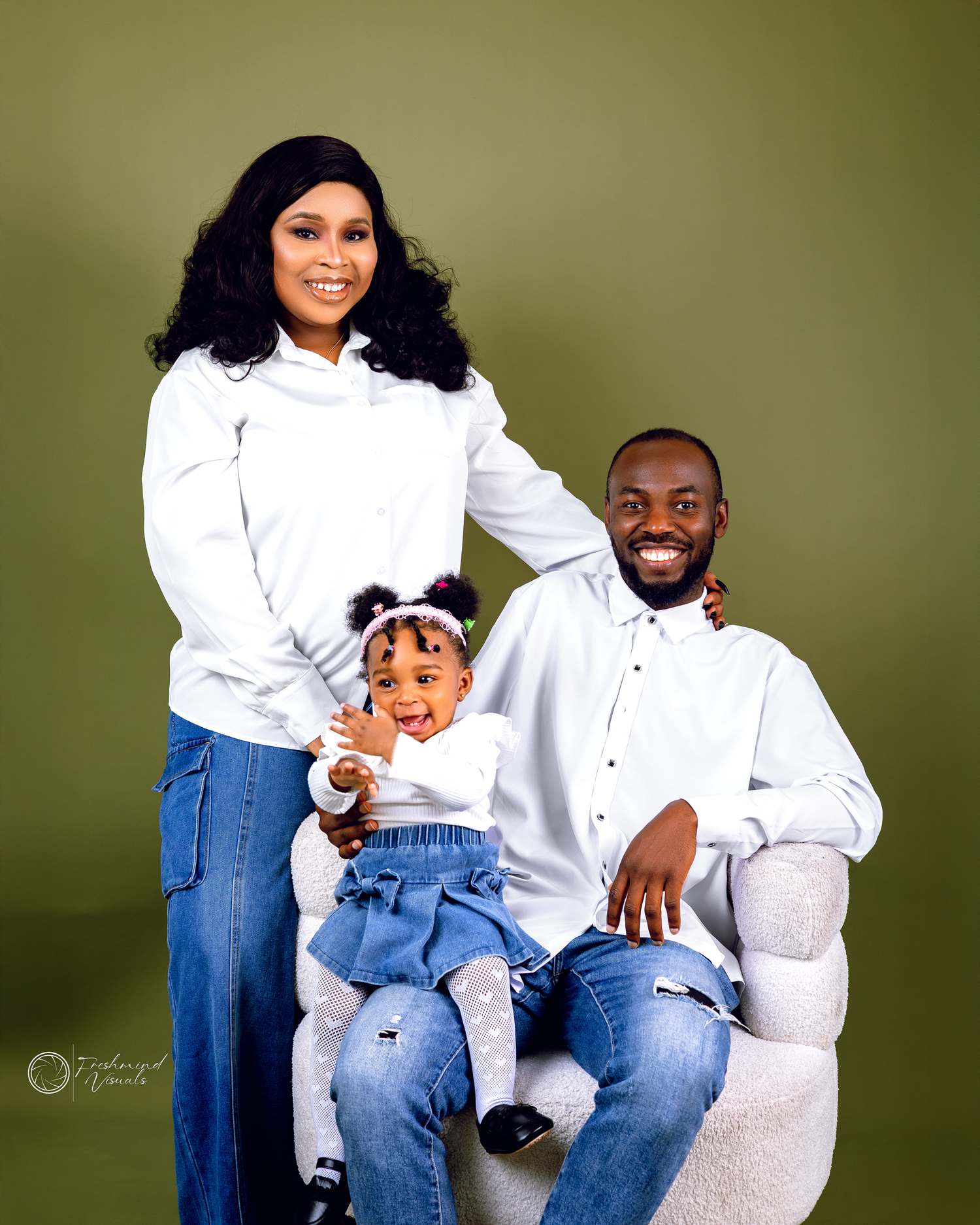 Family in coordinated white and denim outfits poses casually together against olive backdrop.