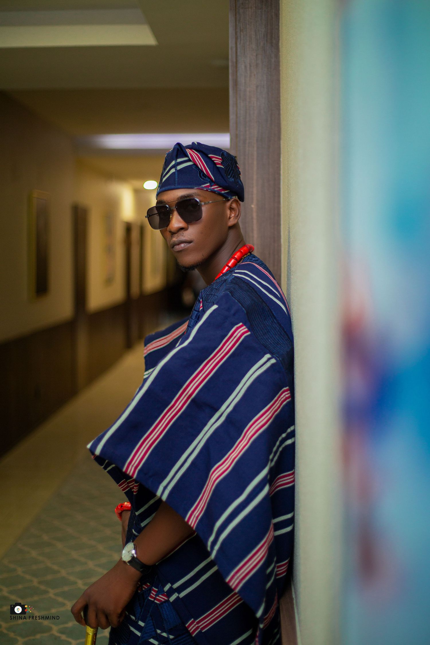 Stylish navy blue agbada with bold stripes photographed in a modern hallway setting.