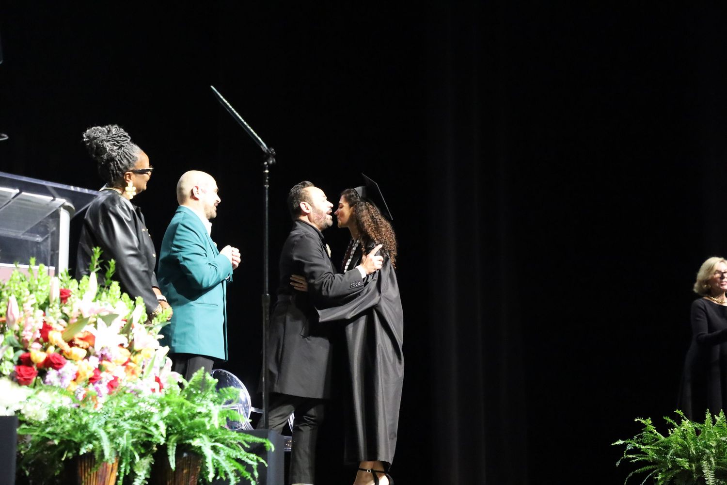 Graduation ceremony stage decorated with green plants and floral arrangements.