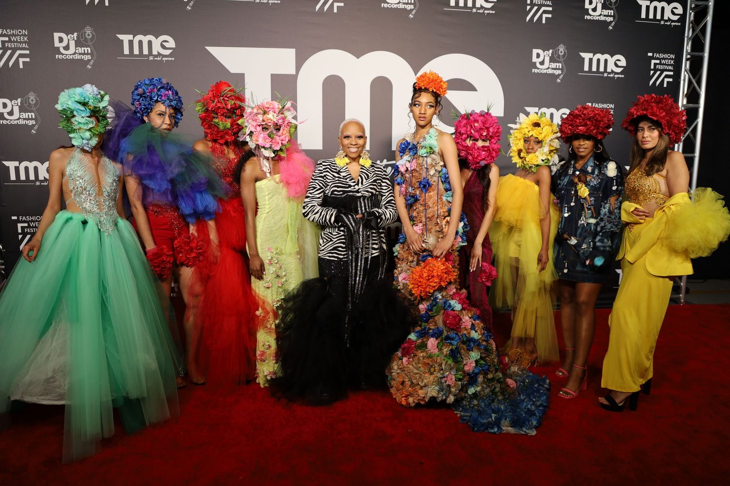 Wide shot of fashion event attendees in vibrant dresses against TME backdrop.