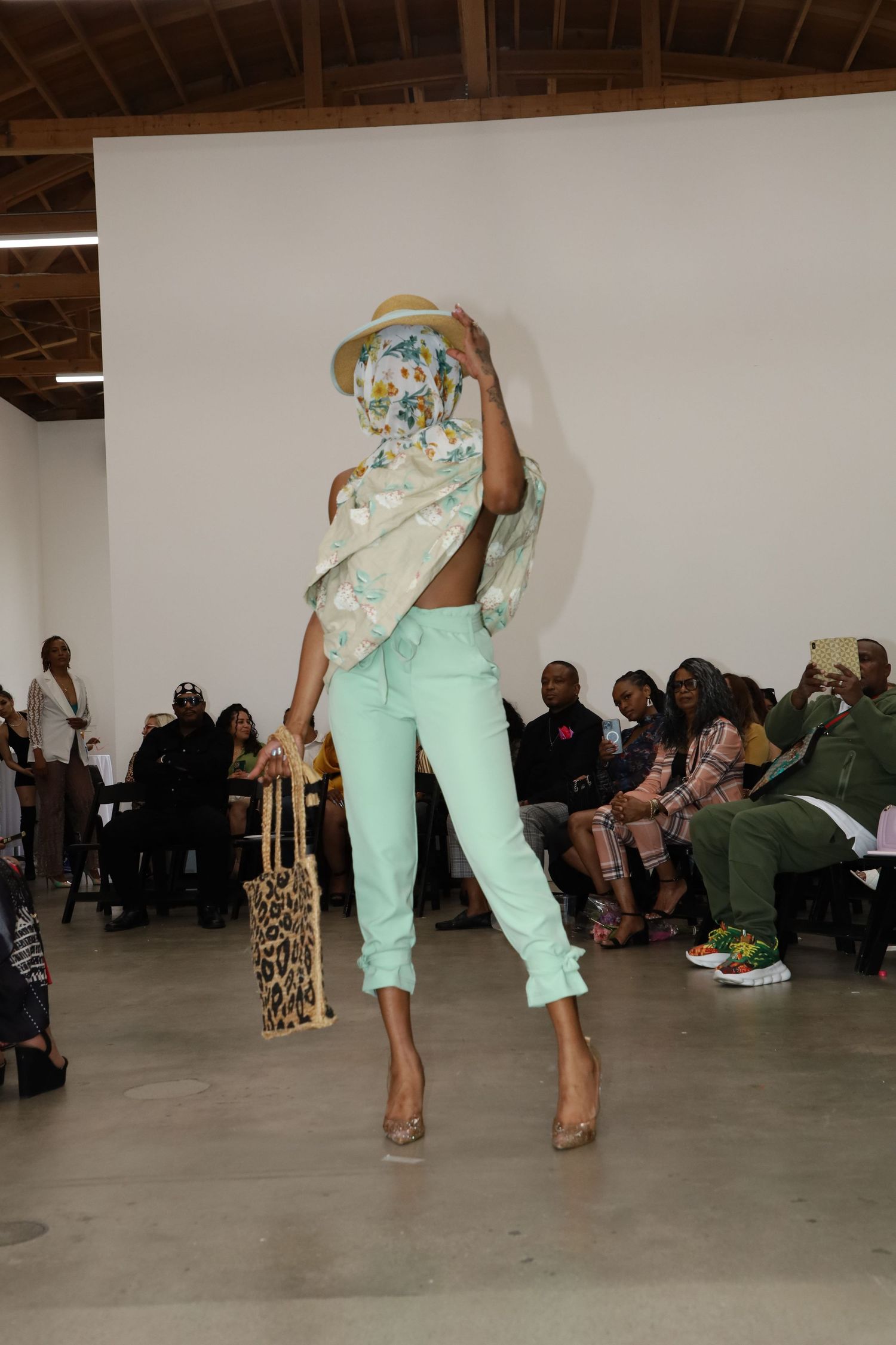 Model showcases mint colored pants and patterned top while performing dance moves at fashion show.