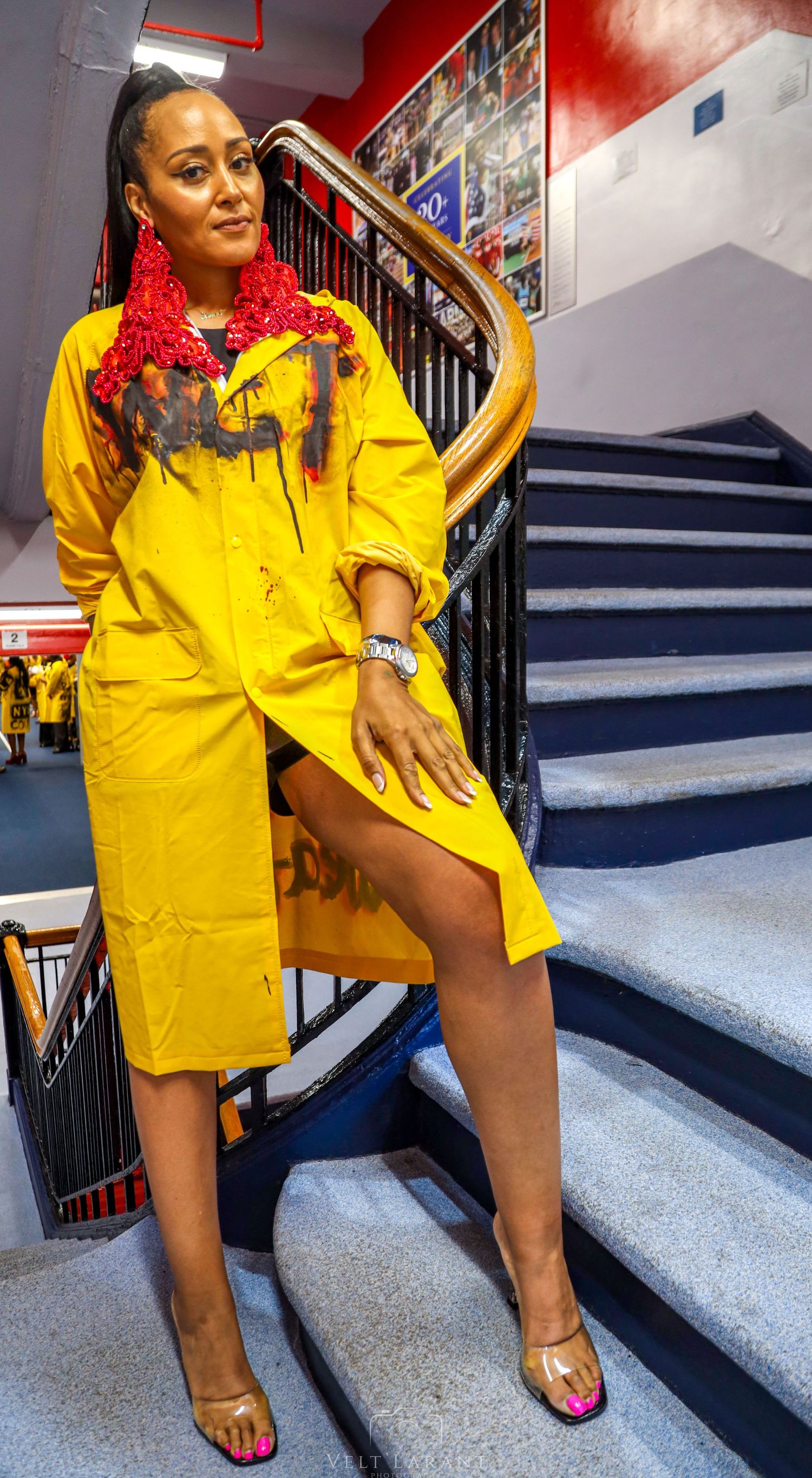 Person in bright yellow jacket poses on blue carpeted stairs.