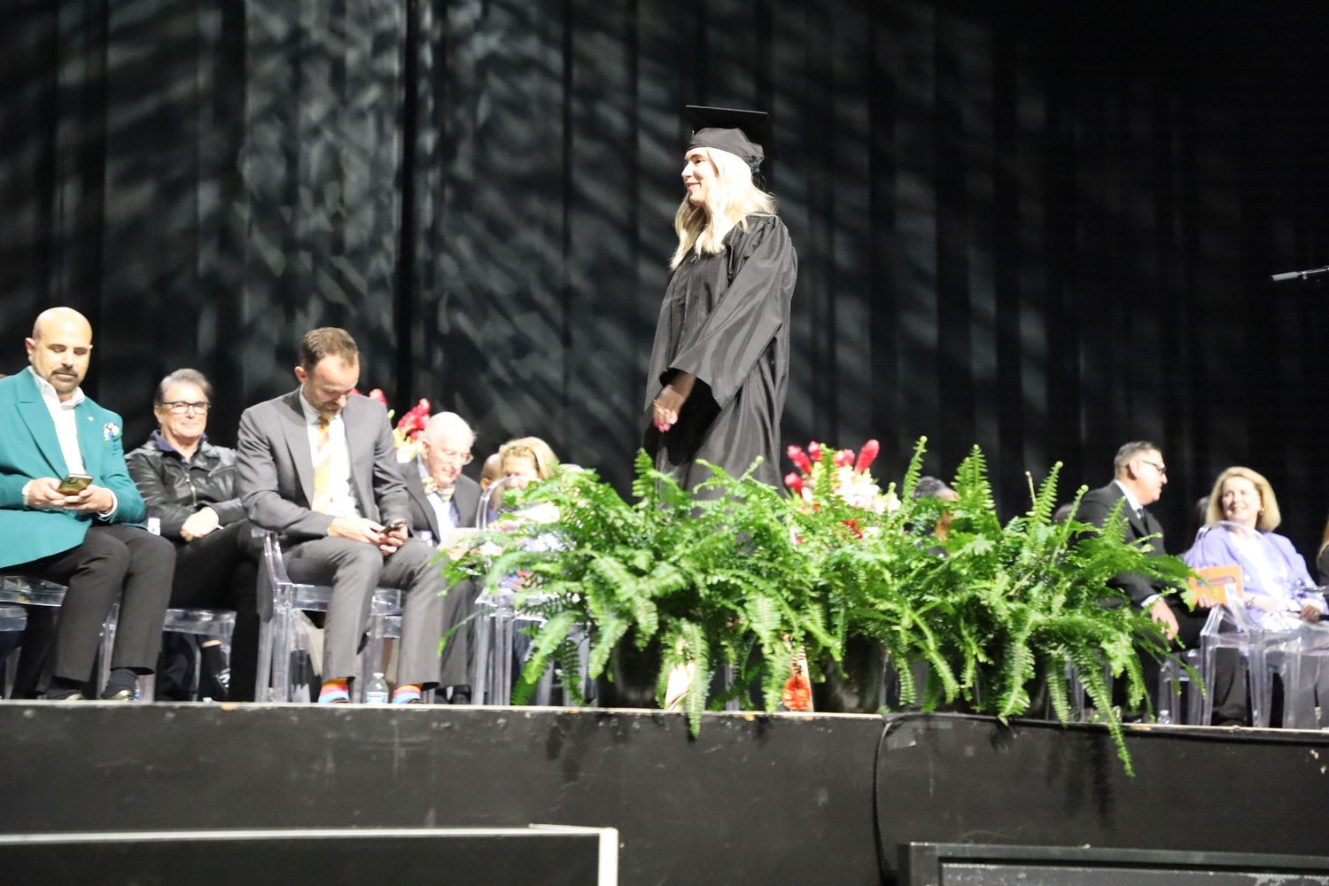 Stage decorated with green ferns and plants for graduation ceremony.