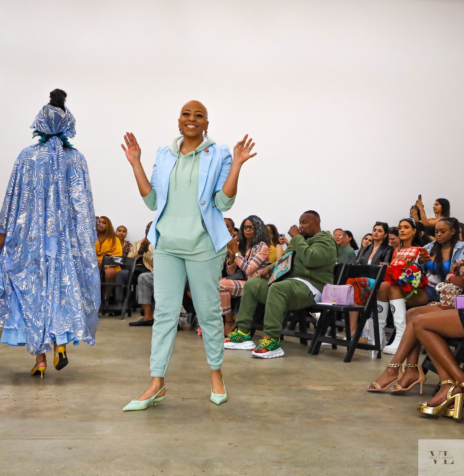 Fashion show featuring pastel colored outfits with audience viewing from both sides.