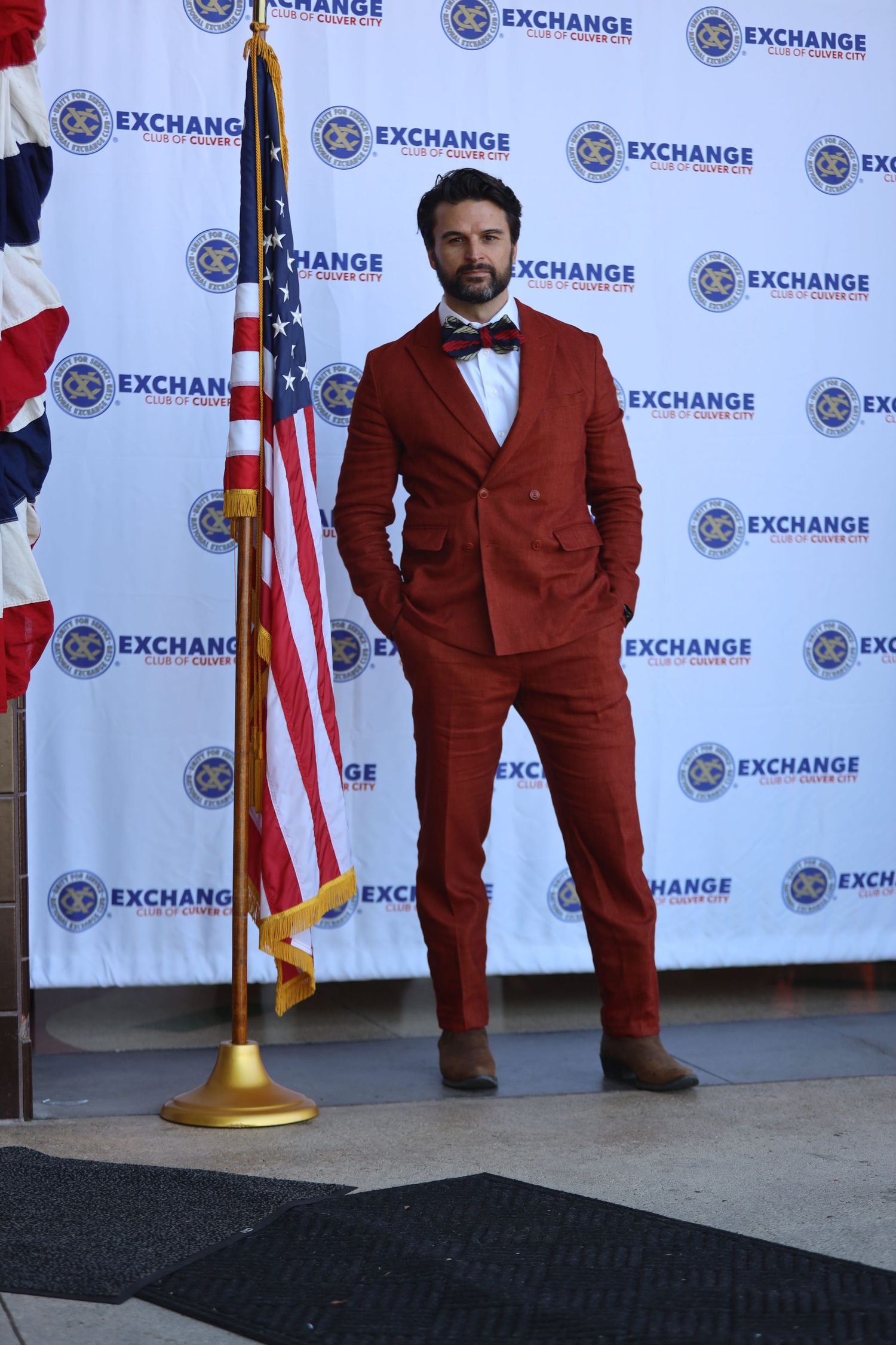 Person in a red suit stands confidently at an Exchange event with American flag display.