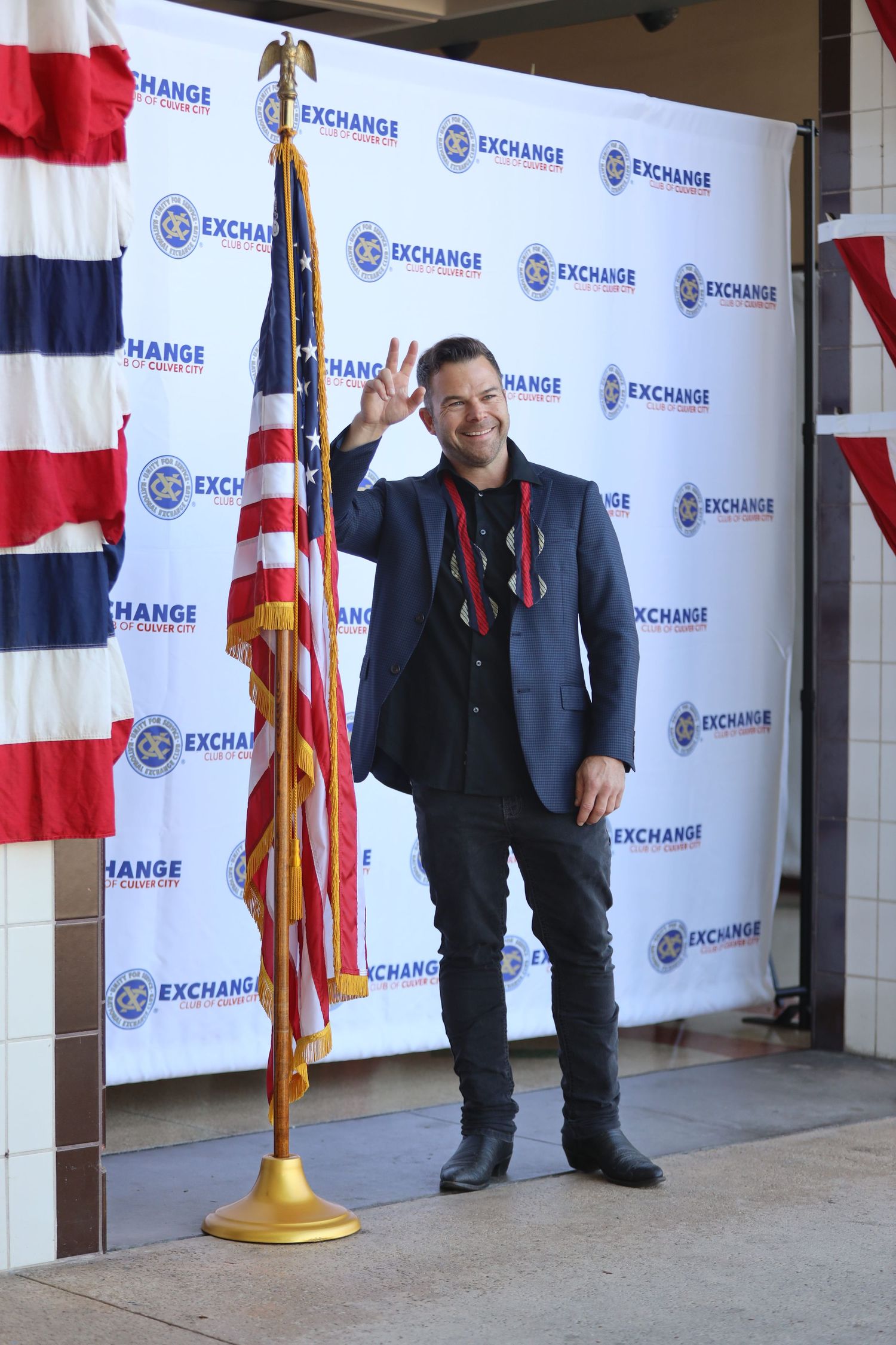 Event setup showing American flags and branded step-and-repeat backdrop with security personnel.
