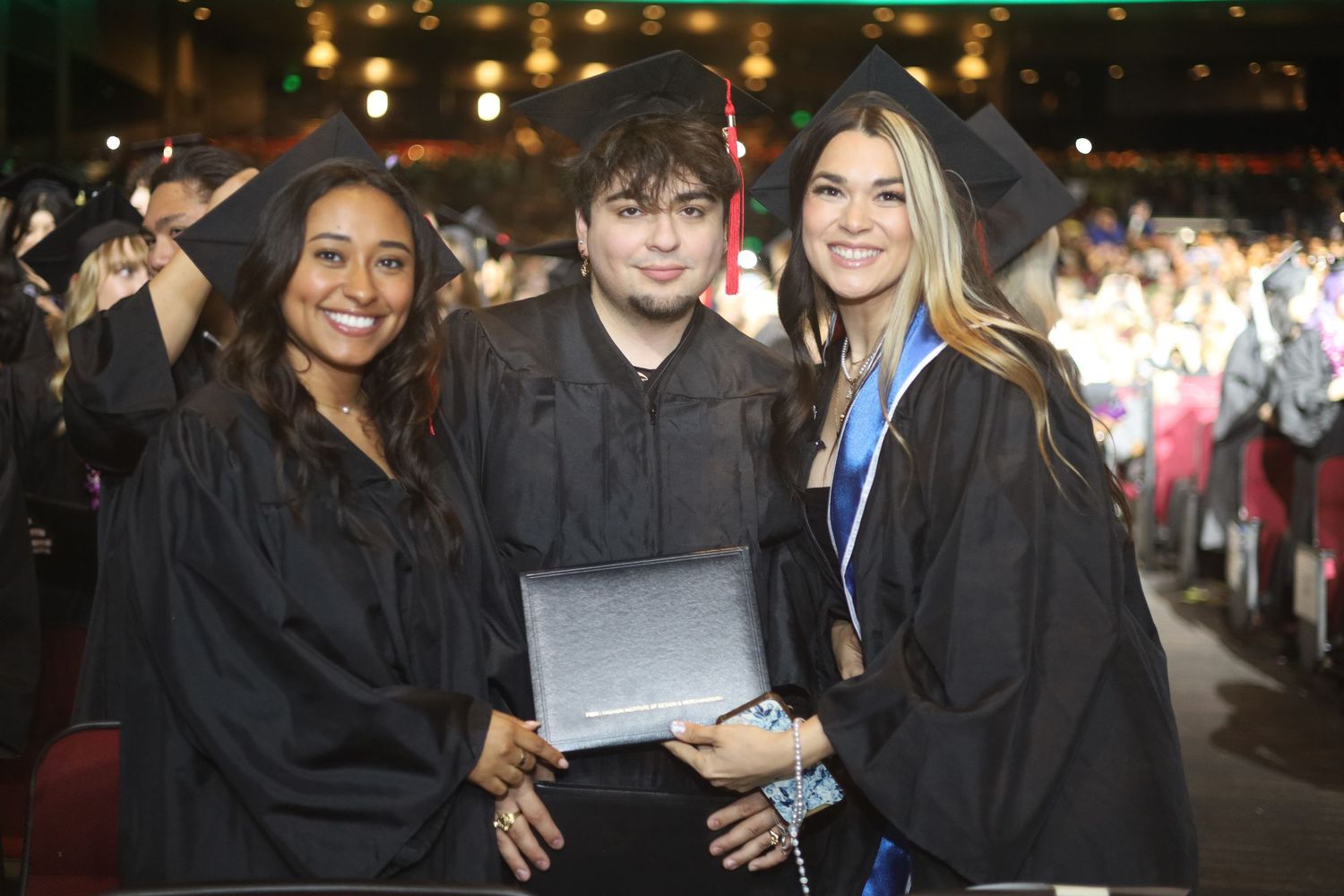 Graduates in academic regalia posing together at indoor graduation ceremony.