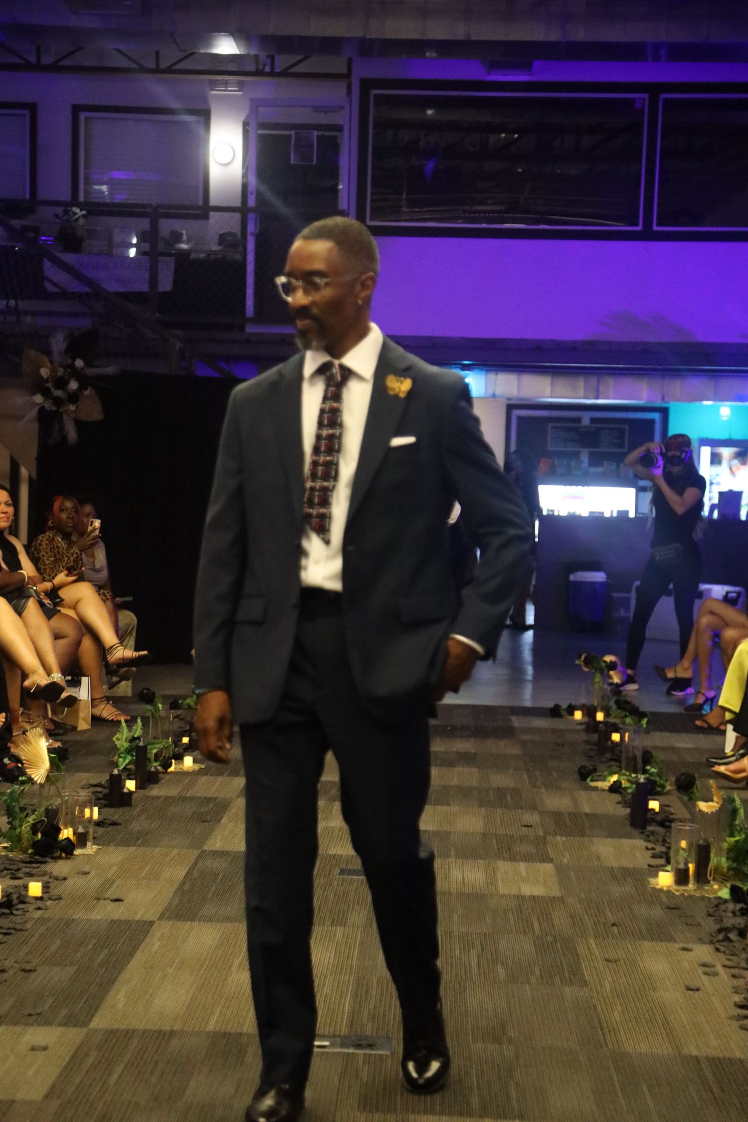 Person in formal suit walking across tiled floor with purple lighting and decorative elements.