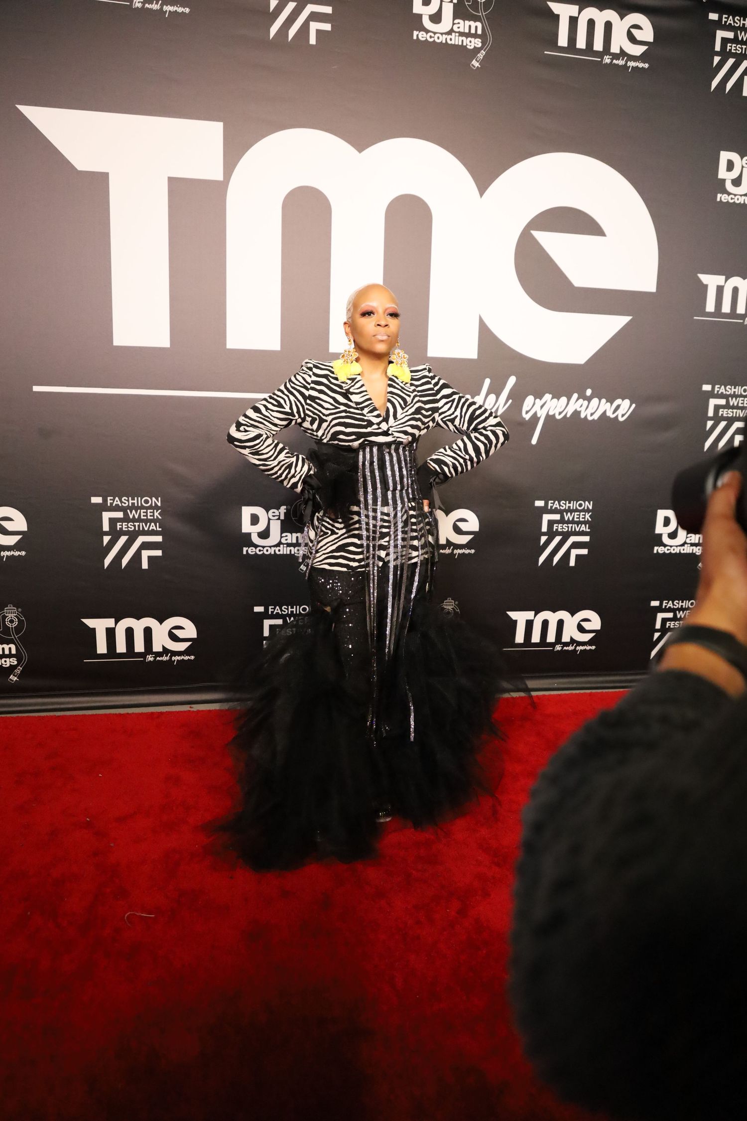 Person in zebra print and black outfit poses on red carpet at TME event.