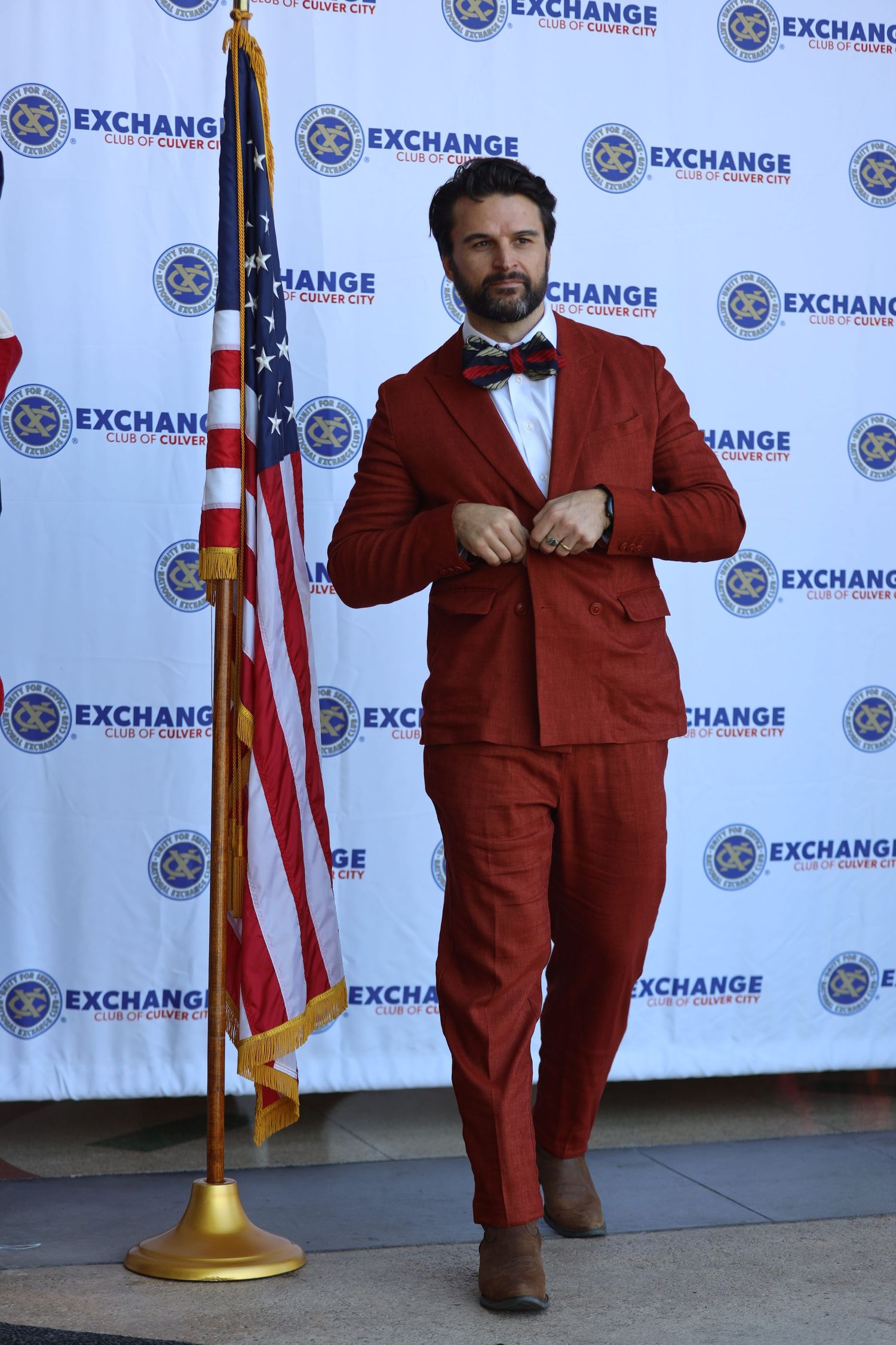 Person wearing burgundy suit strikes pose against Exchange logo backdrop.