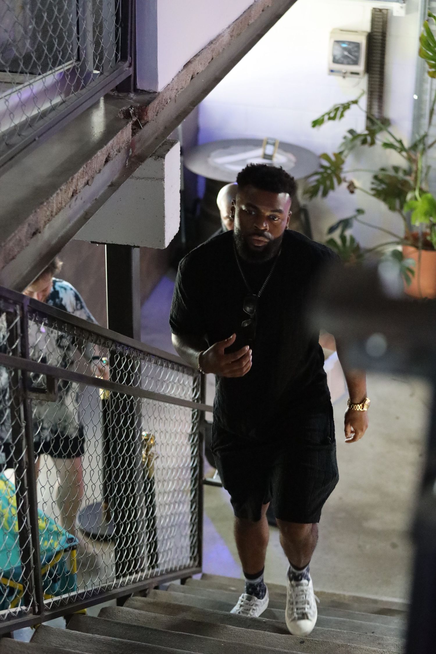 Figure in black clothing ascending industrial staircase in dim lighting.