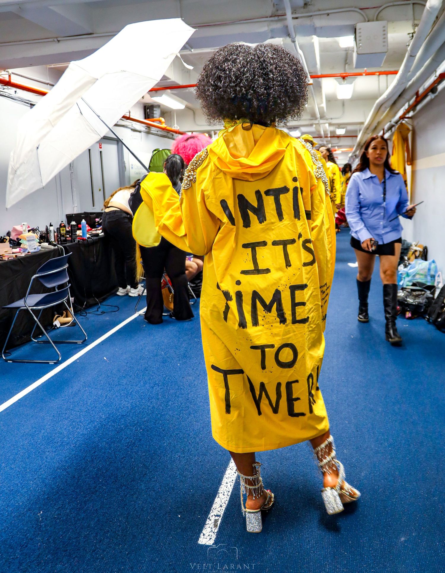 Person in yellow jacket with text written on back walking on blue carpet.