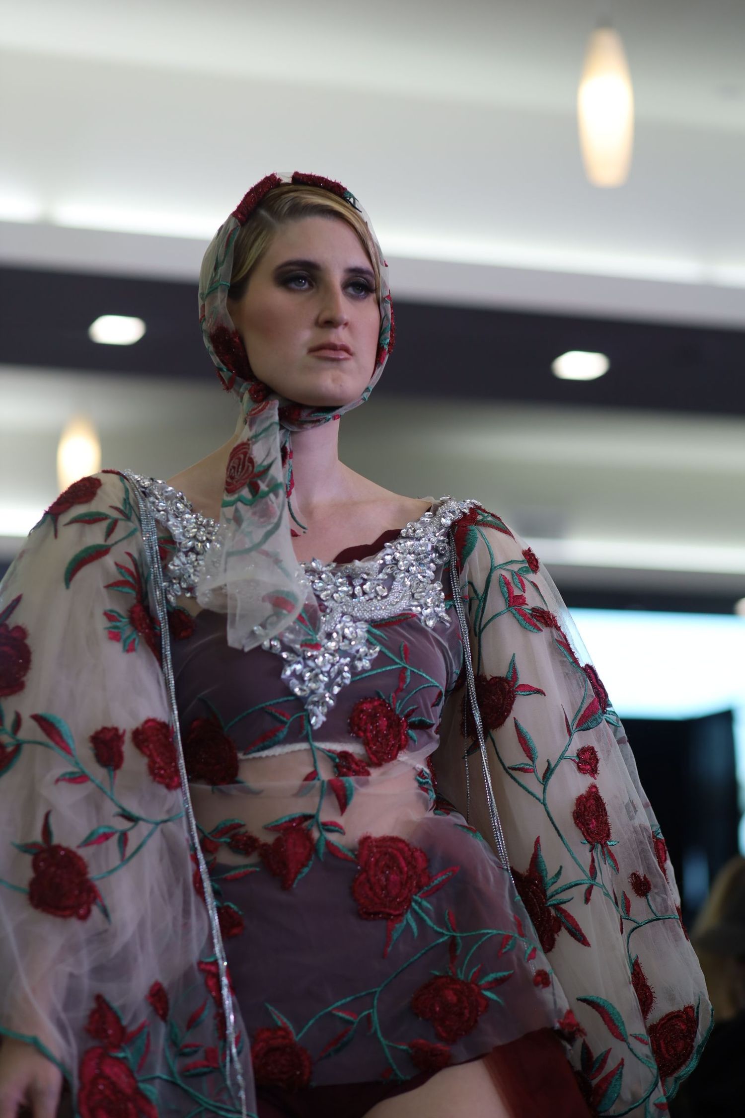 Model showcasing a sheer floral dress with red roses and white lace details on the runway.