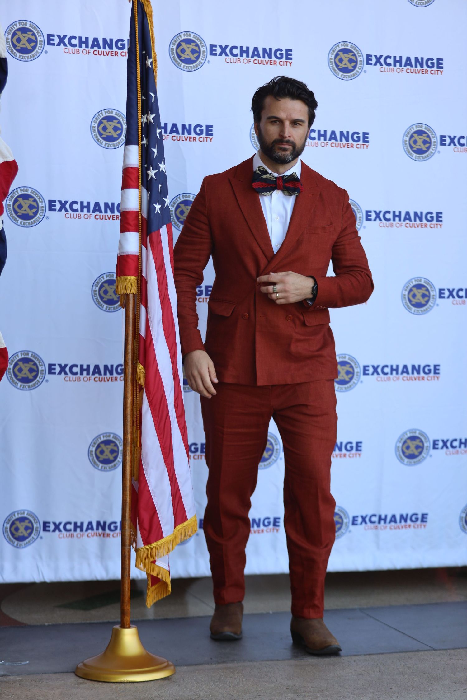 Figure wearing a maroon suit jacket and bowtie poses at an Exchange branded event.