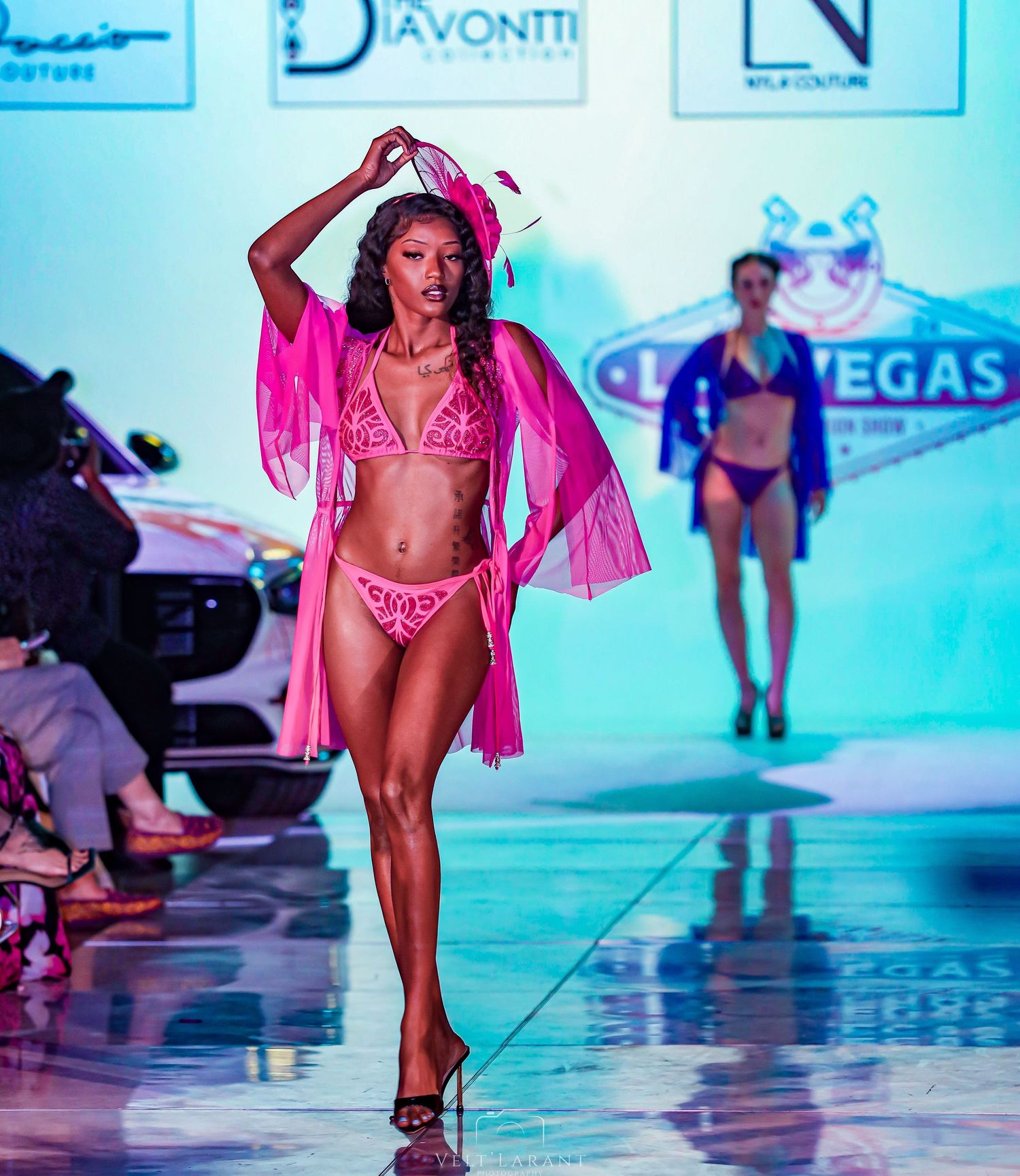 Model showcases pink bikini with flowing sheer robe on illuminated runway.