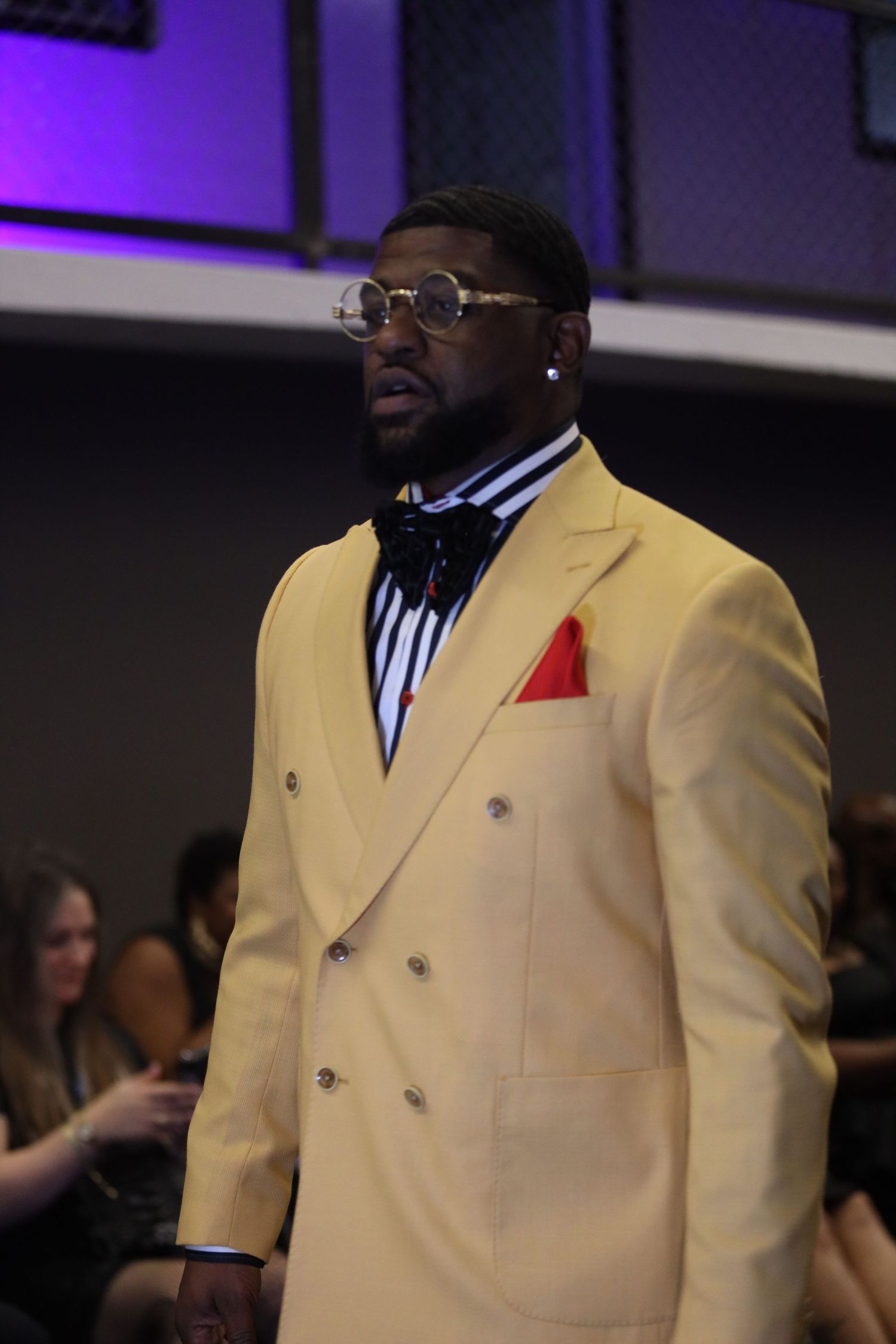 Cream double-breasted suit with red pocket square displayed in fashion show lighting.