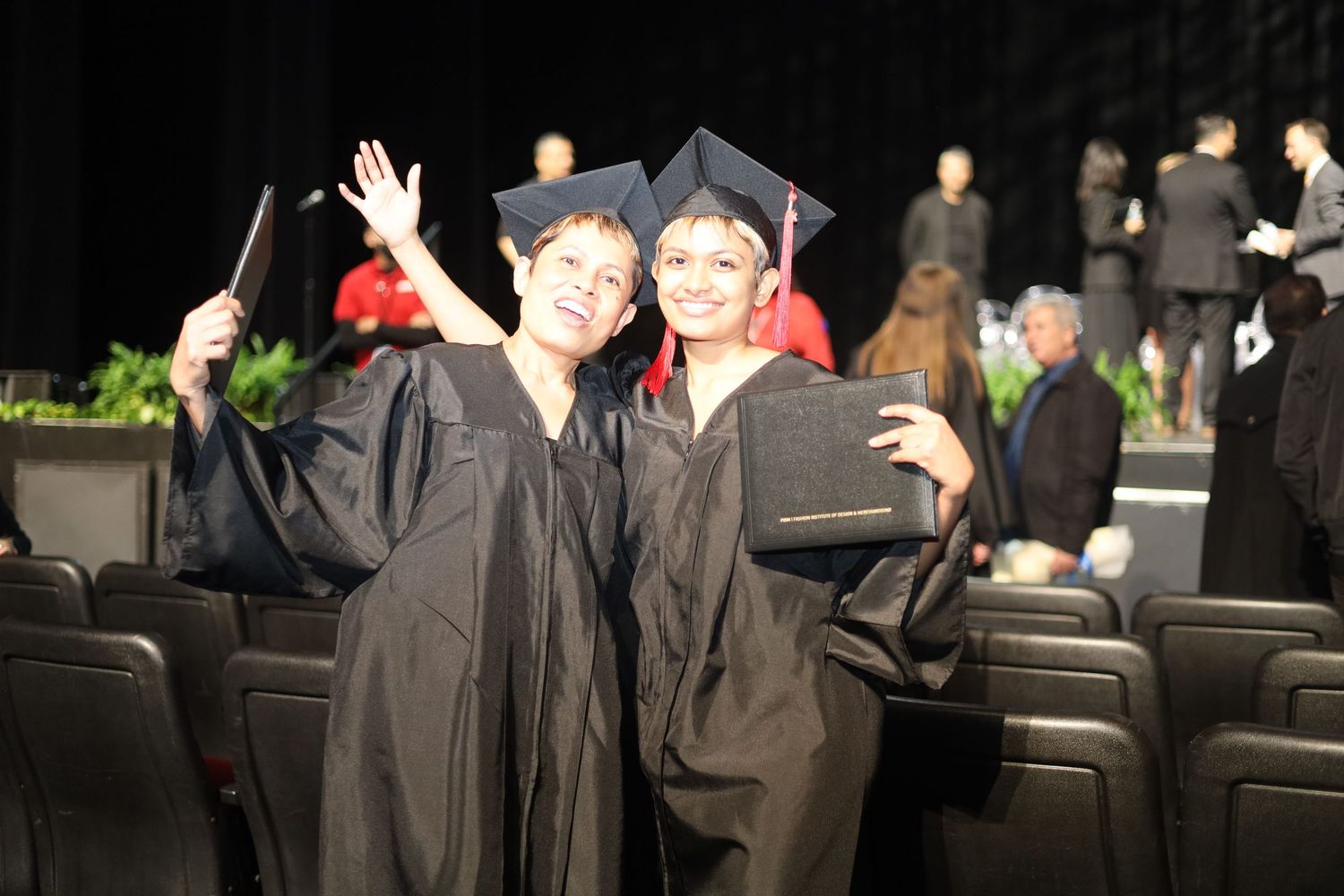 Students in graduation attire wave and celebrate in an auditorium.