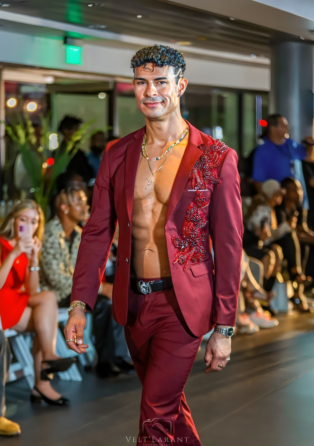 A fashion runway show featuring a burgundy suit design with intricate embroidery details.