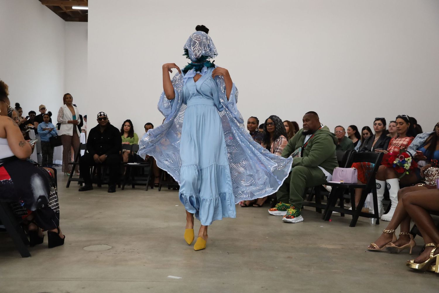 Models walk a minimalist runway space wearing light blue and floral designs.