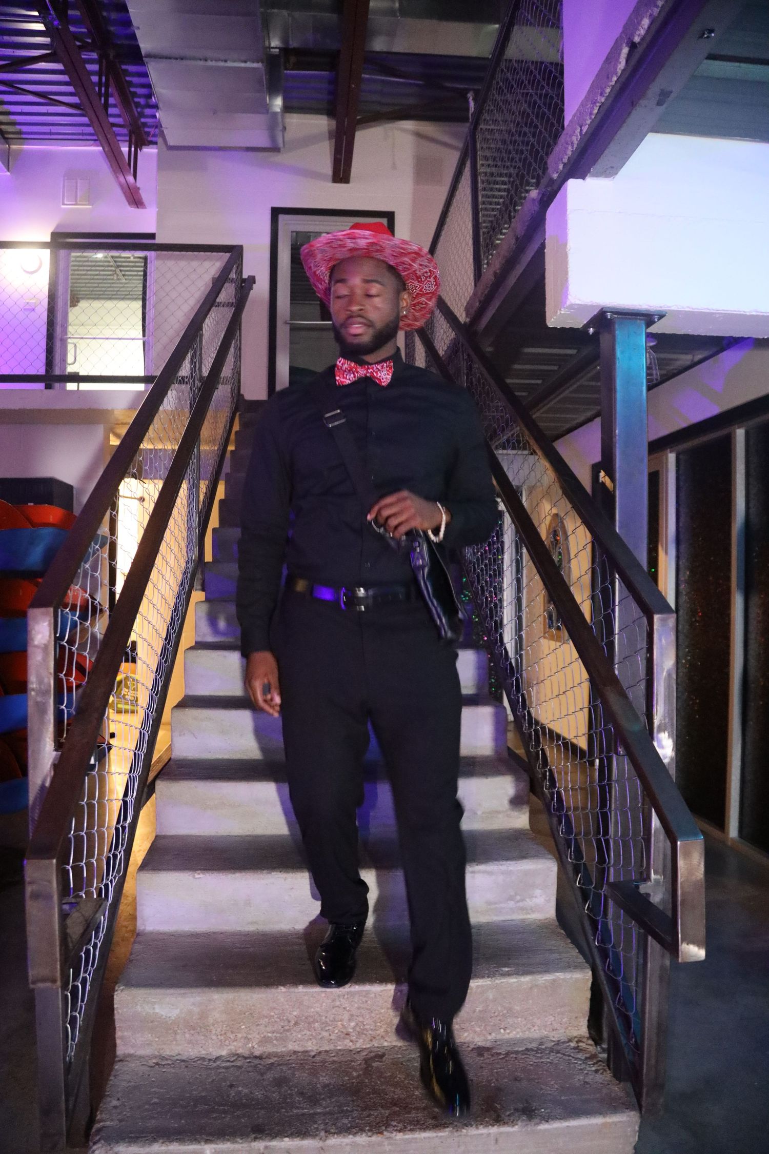 Person in dark clothing walking down stairs with metal railing and red accent lighting.