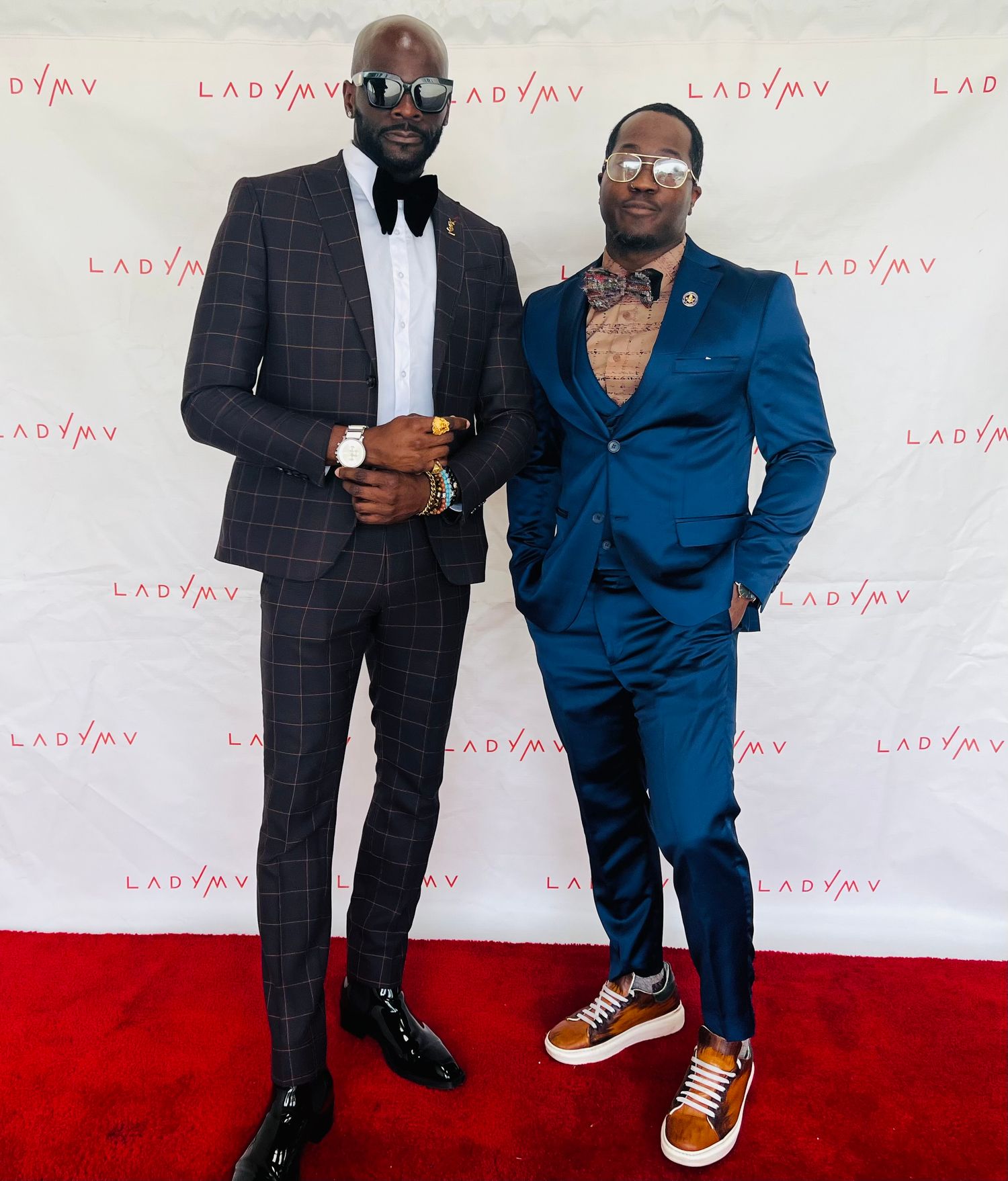 Group poses in formal attire on red carpet with branded backdrop.