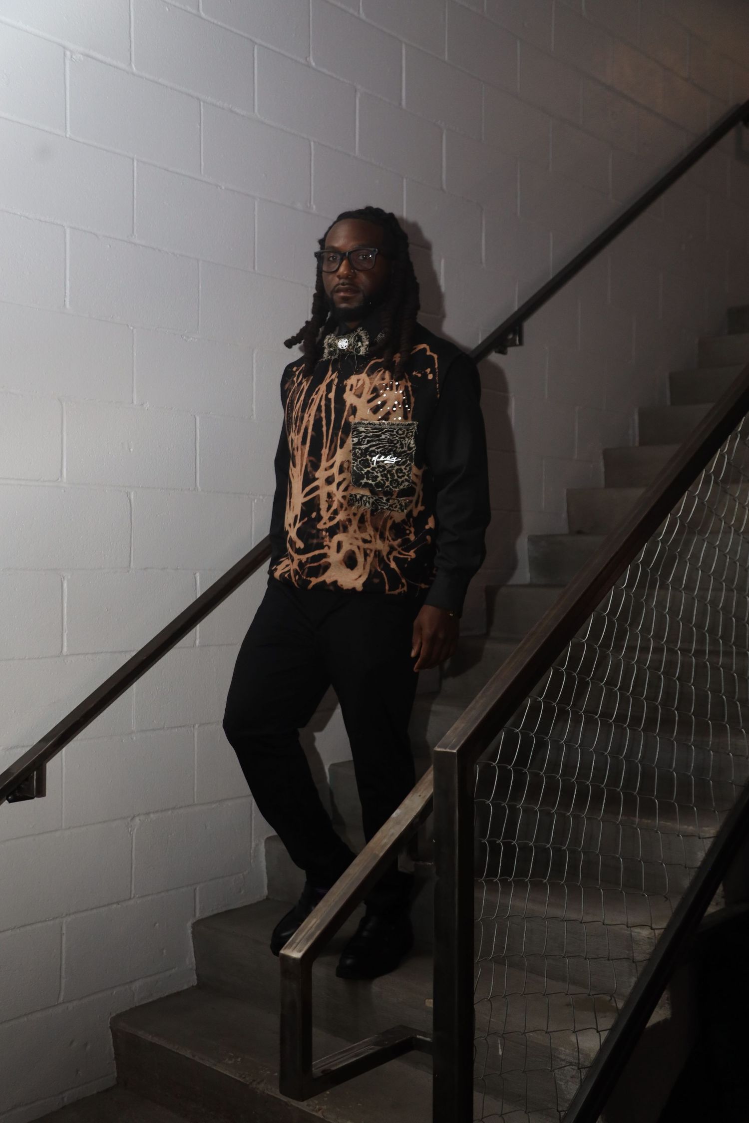 Figure seated on stairs wearing patterned top in dimly lit stairwell.