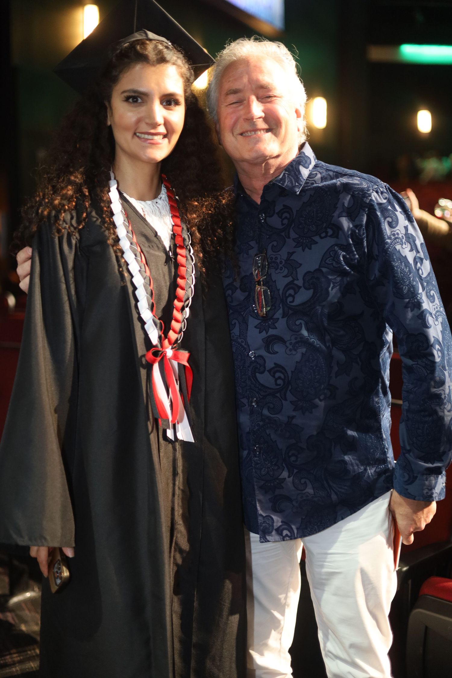 Graduate in cap and gown poses with attendee in navy jacket.