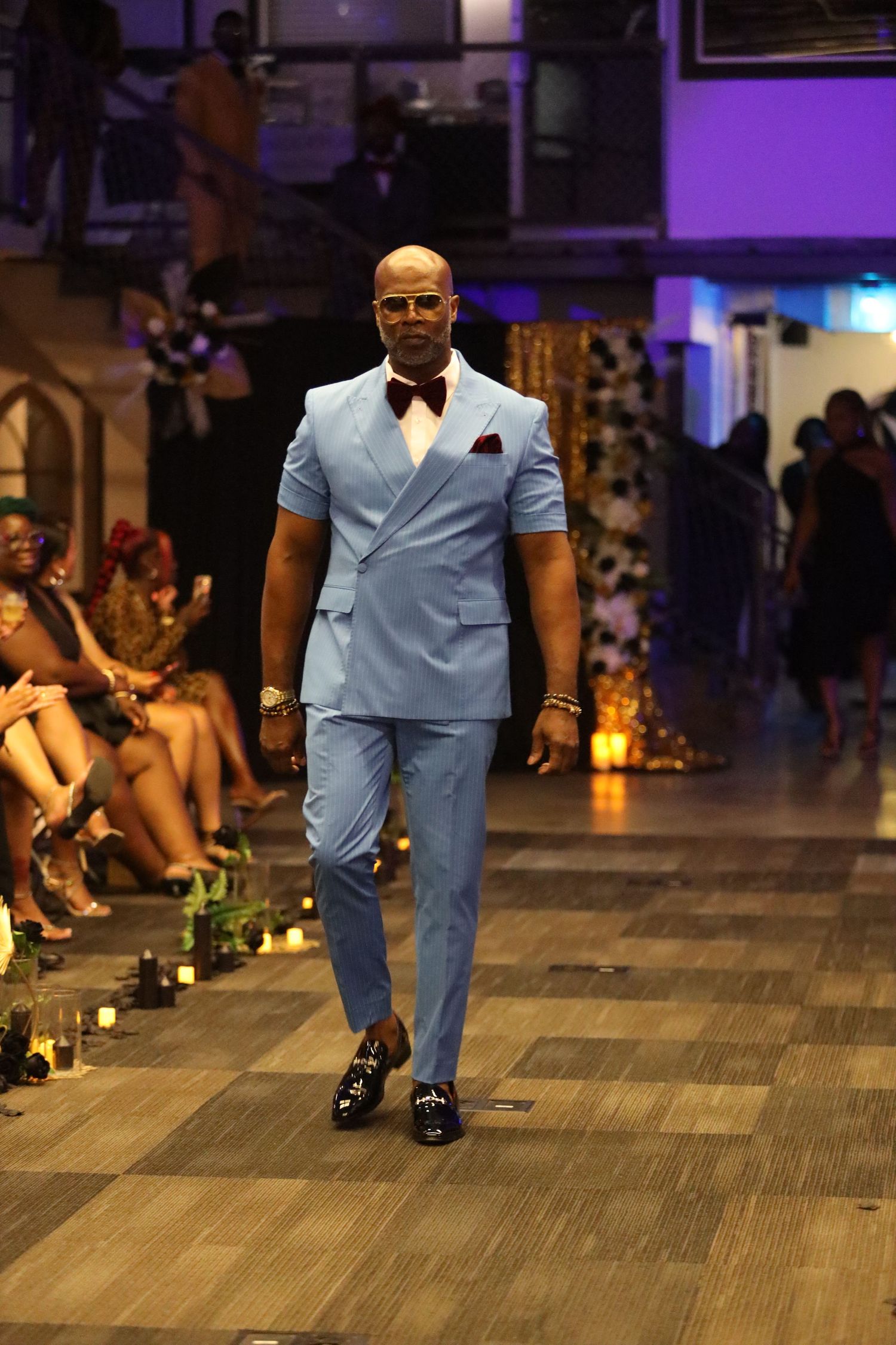Light blue suit with dark accents displayed during fashion show on wooden floor.