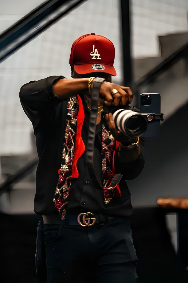 Photographer wearing LA Dodgers cap and Gucci belt captures images with professional camera and stylish floral-trim jacket.
