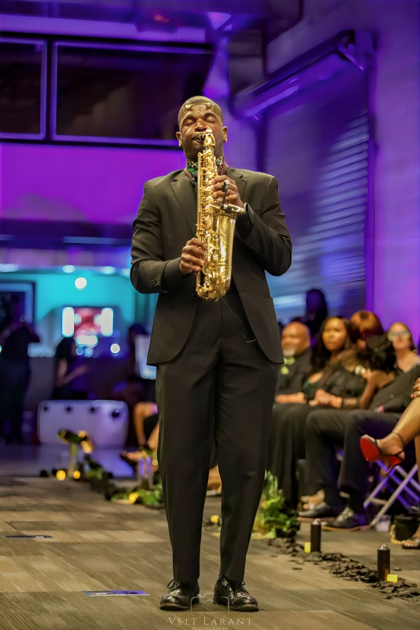 A saxophone performance on stage with purple lighting and an audience in the background.